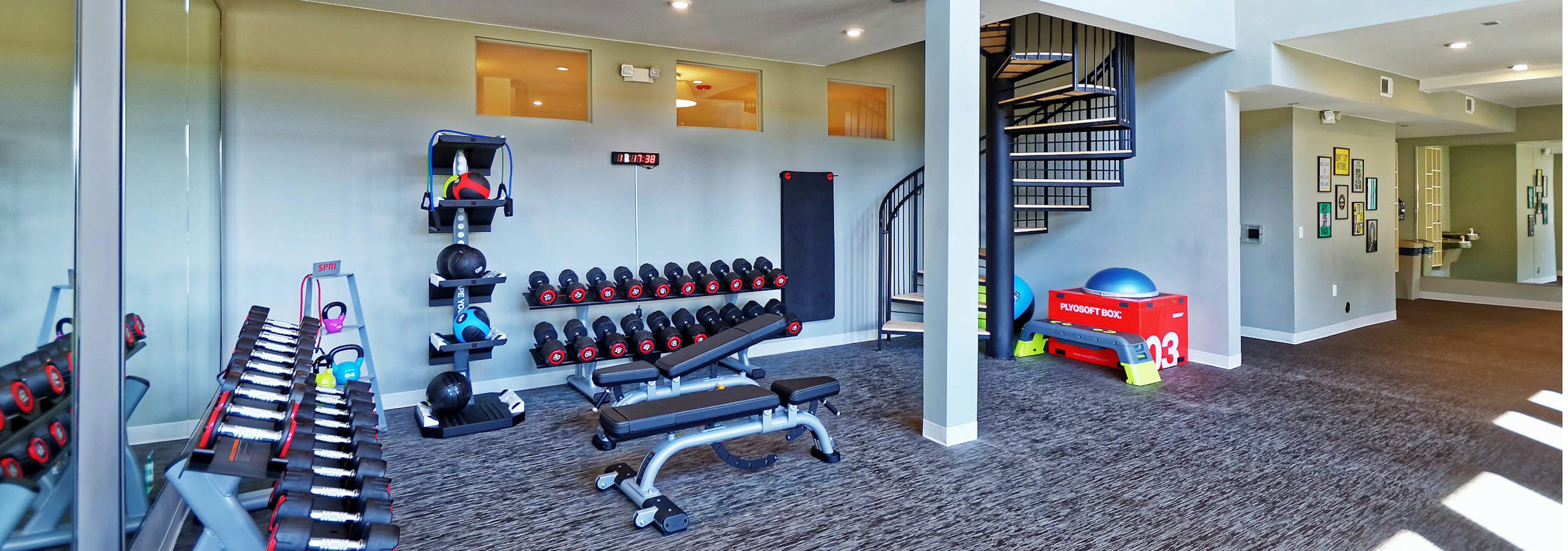 The fitness center at AMLI Dry Creek apartments with a variety of free weights and a spiral staircase and view of hallway