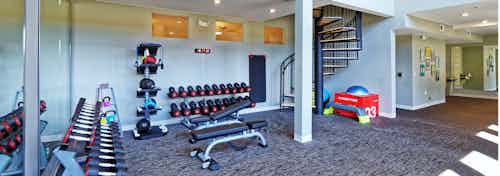The fitness center at AMLI Dry Creek apartments with a variety of free weights and a spiral staircase and view of hallway
