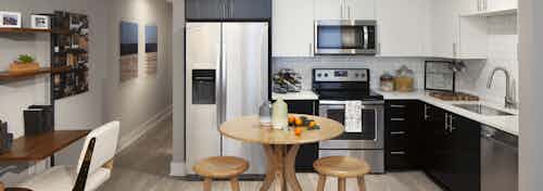 A kitchen in an apartment at AMLI Riverfront Green with a small table and an office desk as well as a view of the hallway