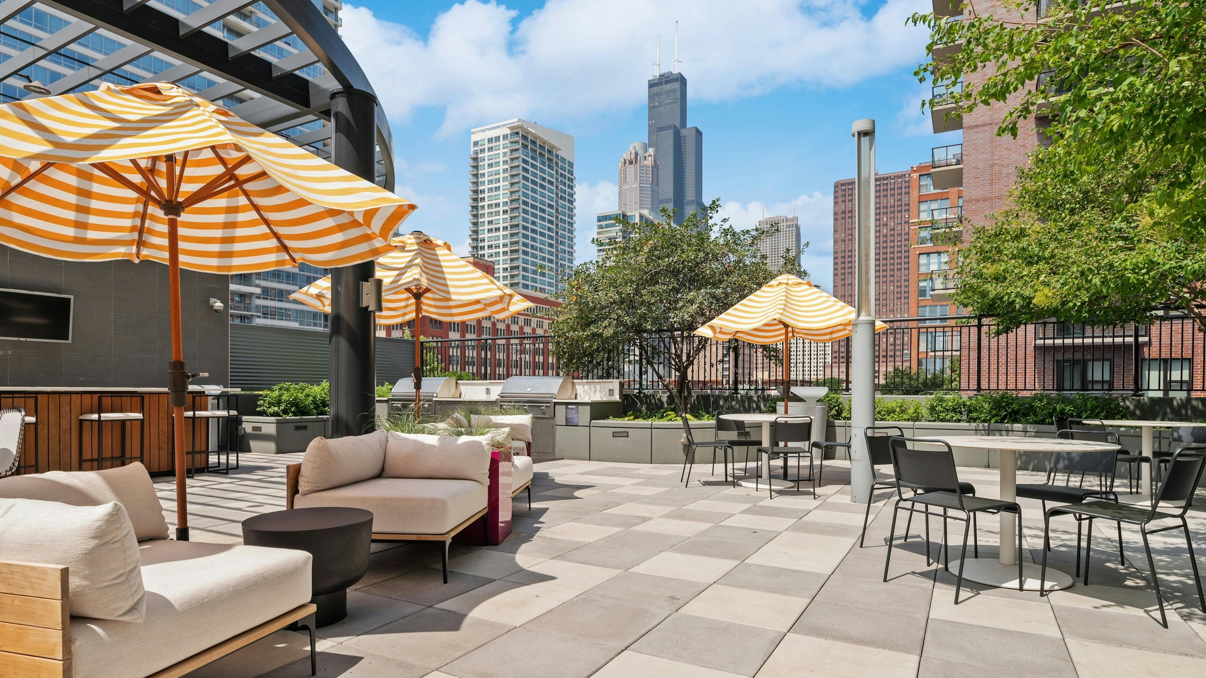AMLI Lofts amenity deck with shaded patio furniture and dining tables near grilling station with view of city buildings