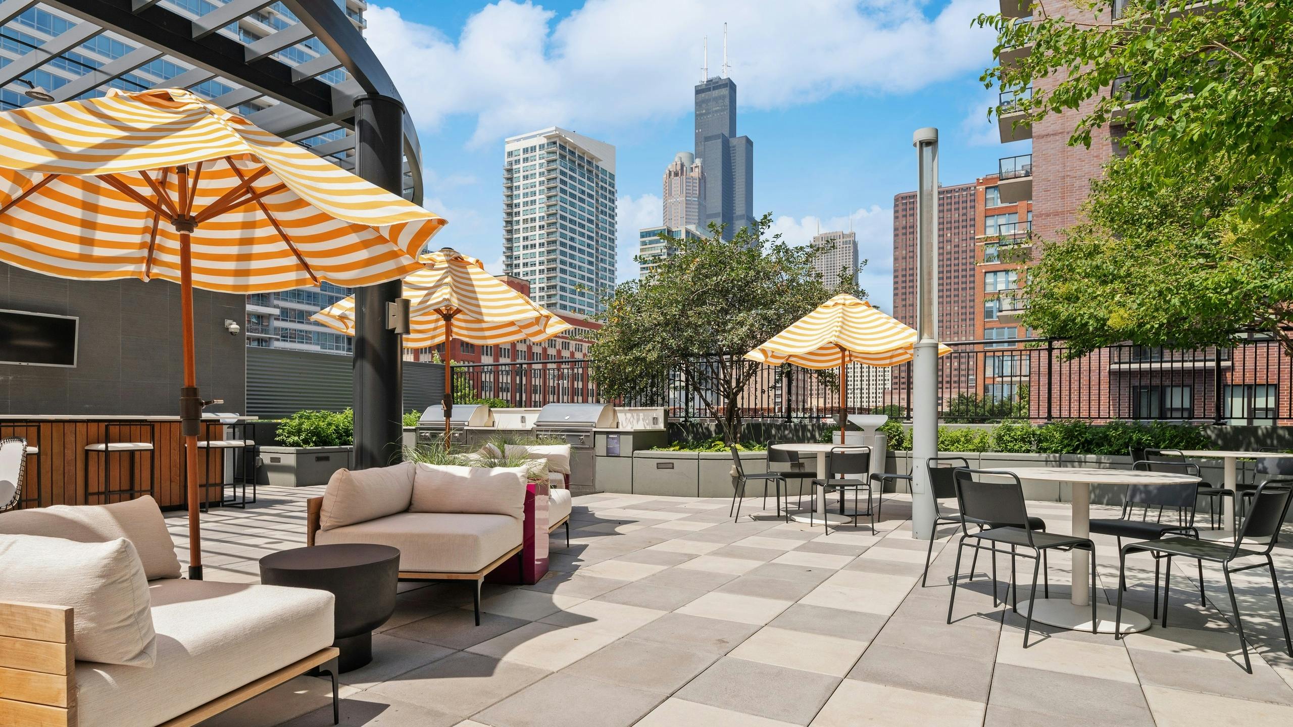AMLI Lofts amenity deck with shaded patio furniture and dining tables near grilling station with view of city buildings