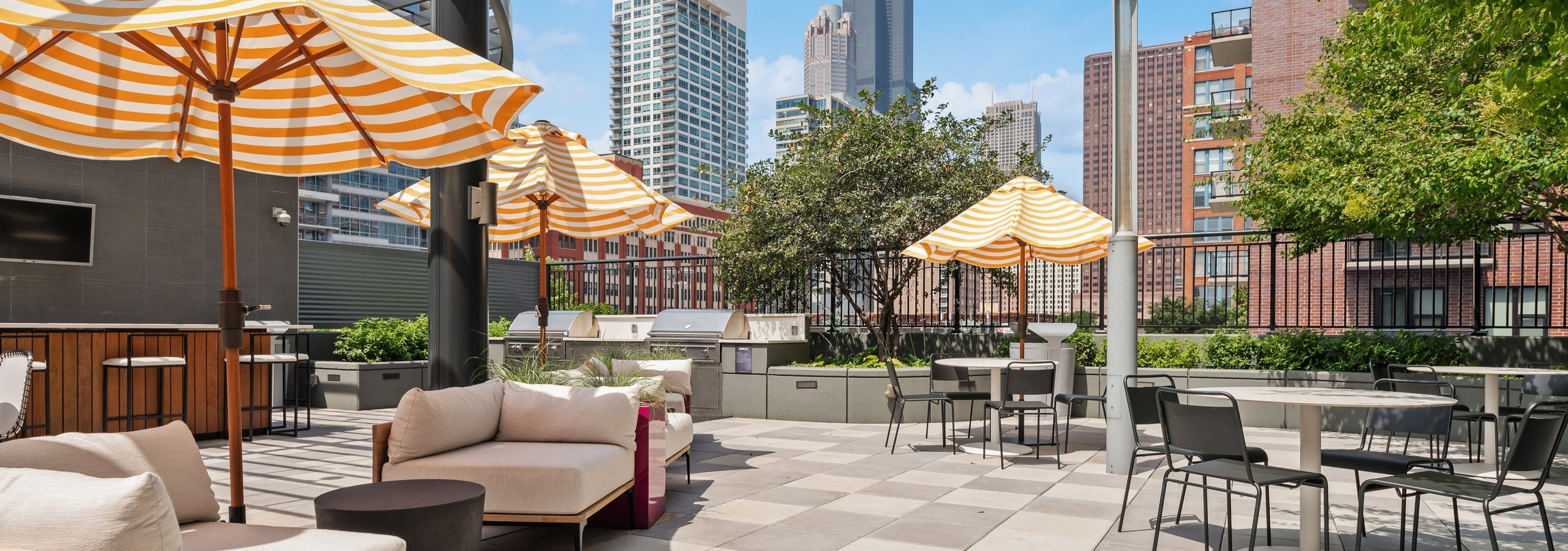 AMLI Lofts amenity deck with shaded patio furniture and dining tables near grilling station with view of city buildings