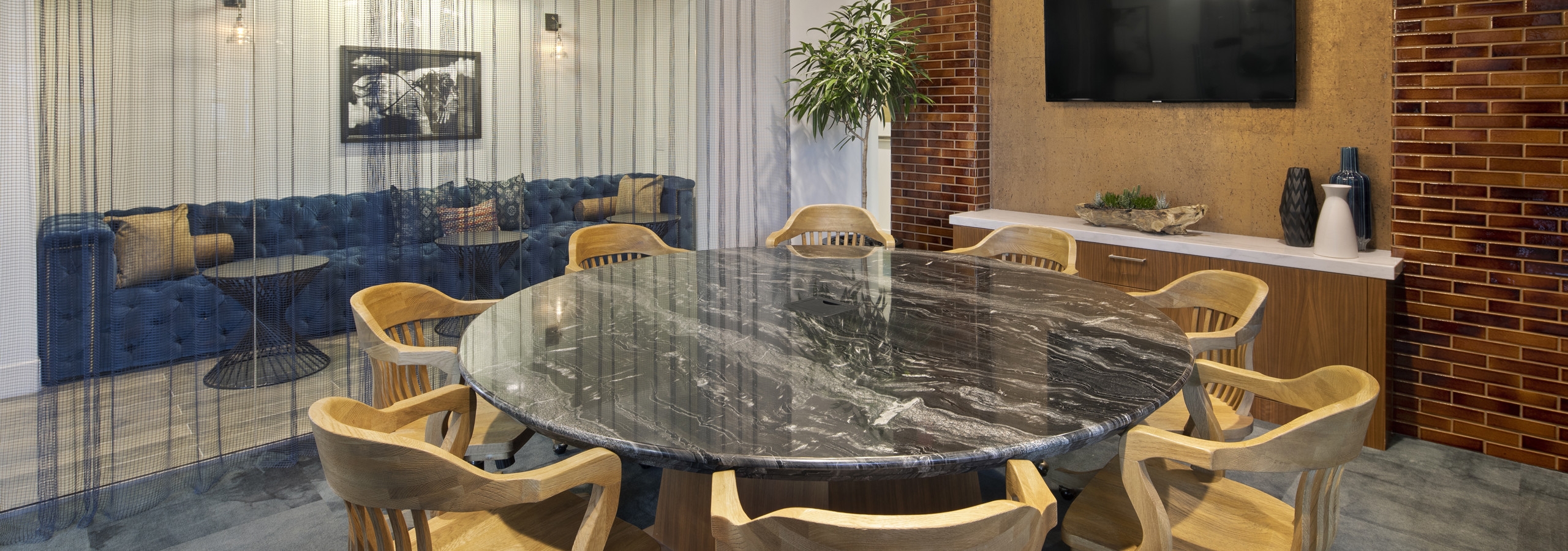 Interior of AMLI Marina Del Rey apartment conference room with round marble table, glass walls with sheer curtains and TV