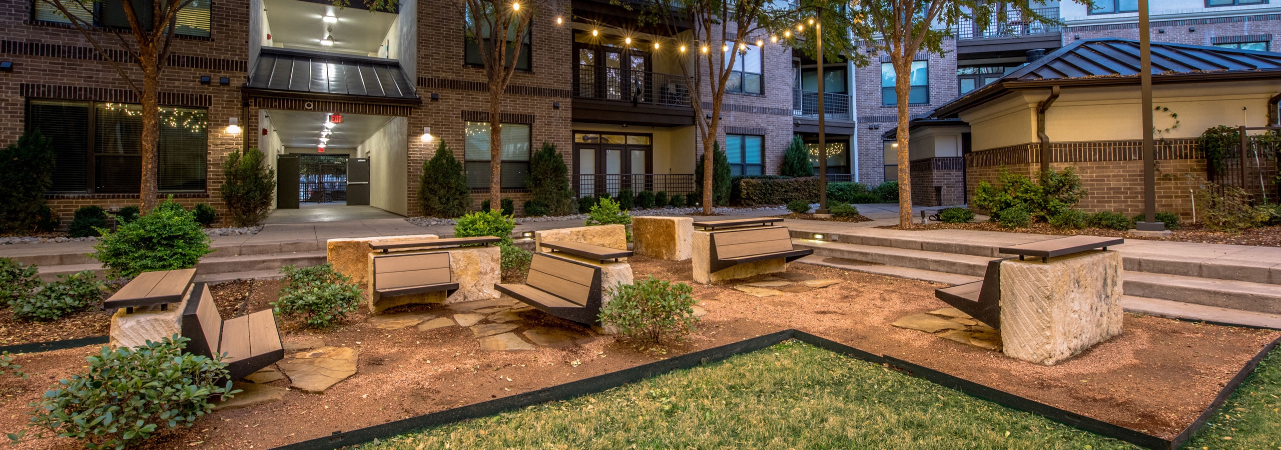 Nighttime courtyard with grass and seating and landscaping and buildings in background at AMLI at the Ballpark apartments