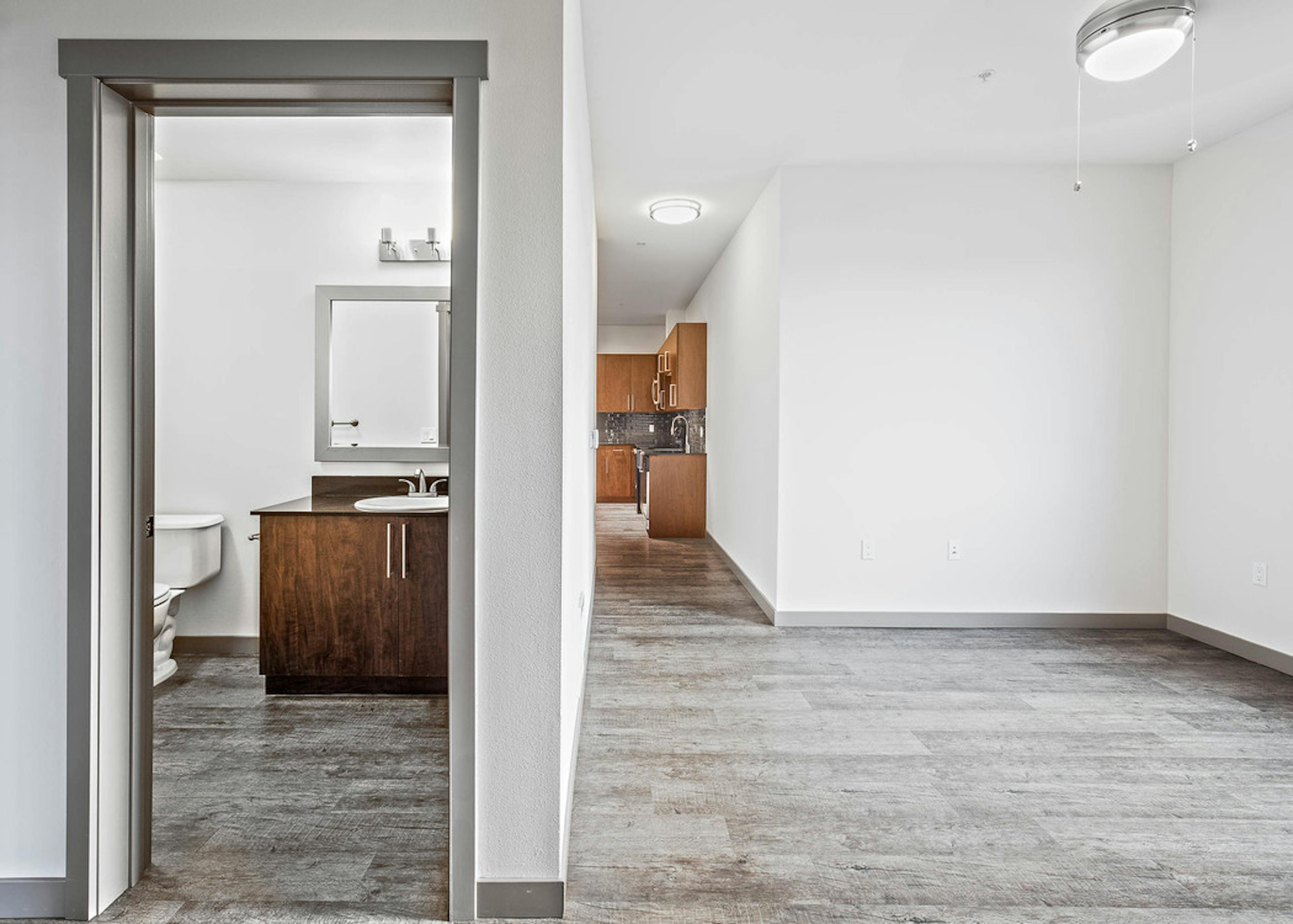 Interior view of bathroom and kitchen from the living room of a AMLI Mark24 apartment with dark cabinets light floors 