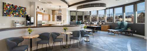 The club room at AMLI Inverness apartments showcasing several padded chairs and tables and a kitchen area and window views