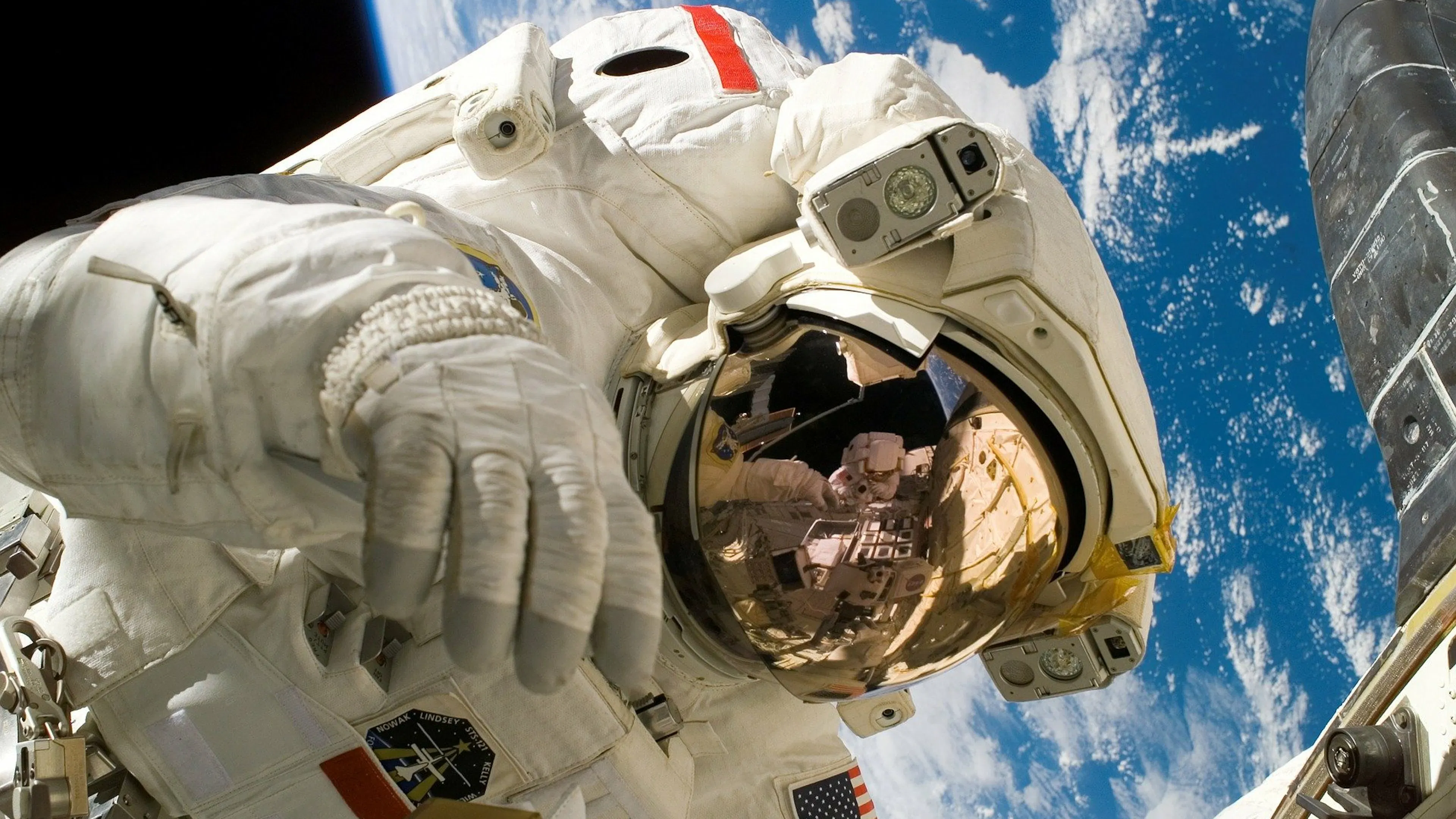 An astronaut's visor reflecting the ISS while floating in orbit above Earth