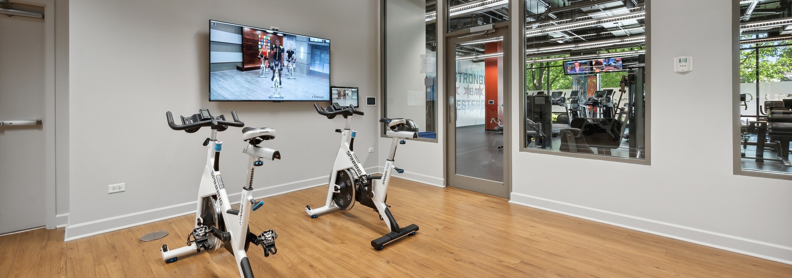 The yoga and spin room at AMLI 900 with two spin bikes and flat screen TV and view to fitness center