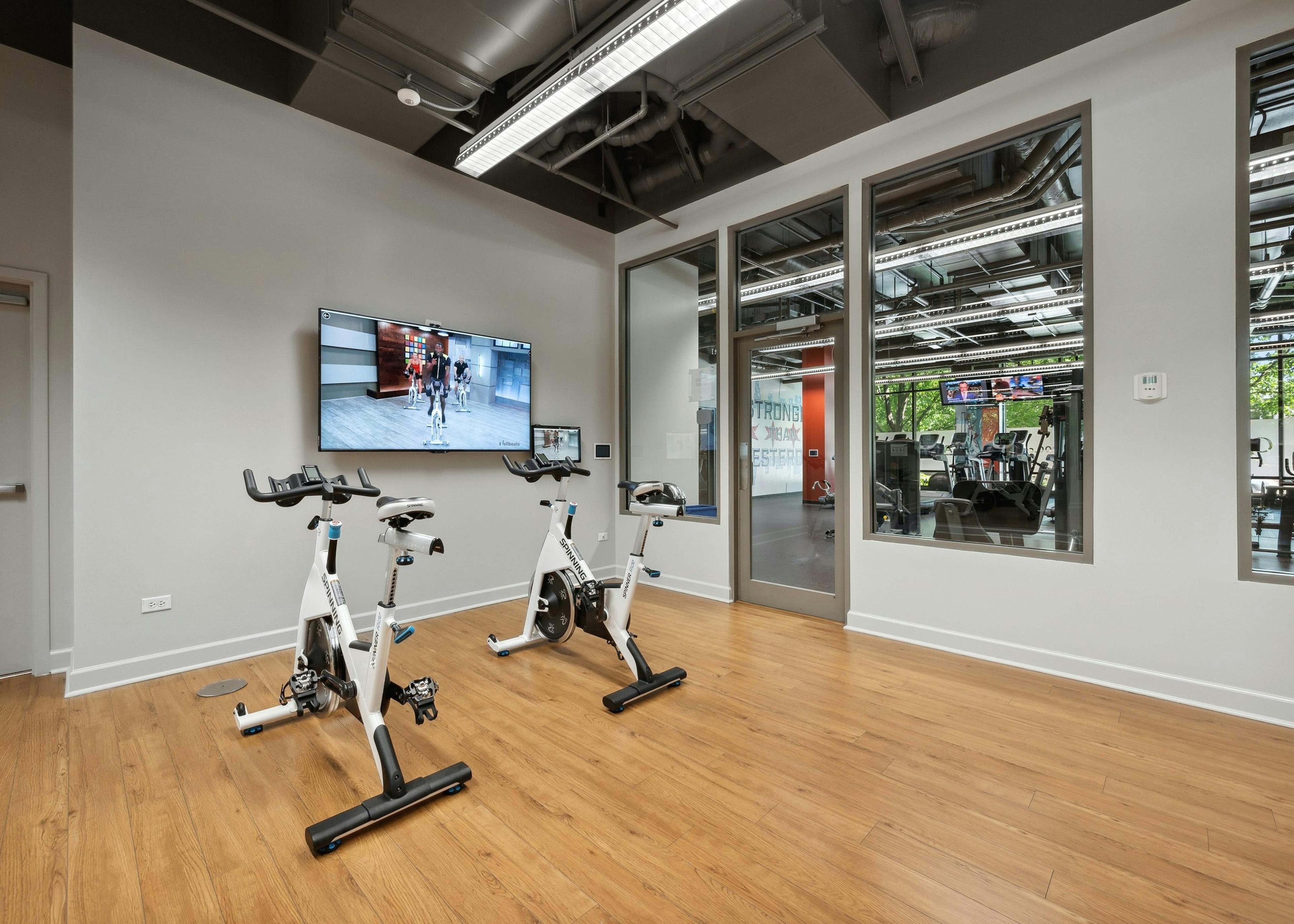 The yoga and spin room at AMLI 900 with two spin bikes and flat screen TV and view to fitness center