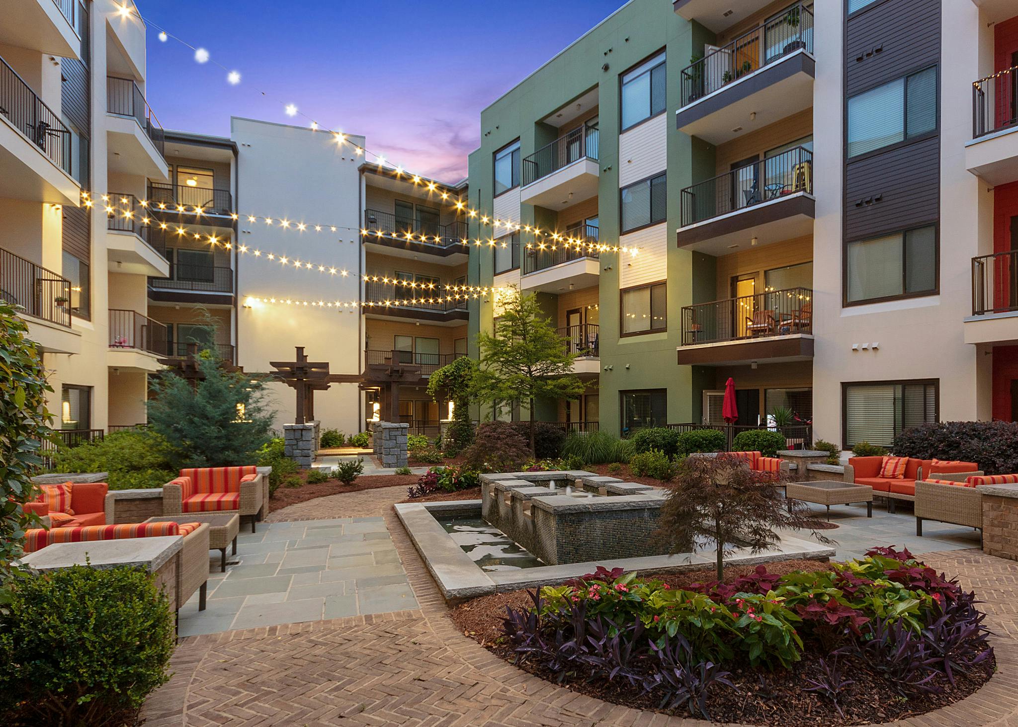 Nighttime exterior of AMLI Ponce Park courtyard with sitting area and fountain and hanging lights with colorful flowers
