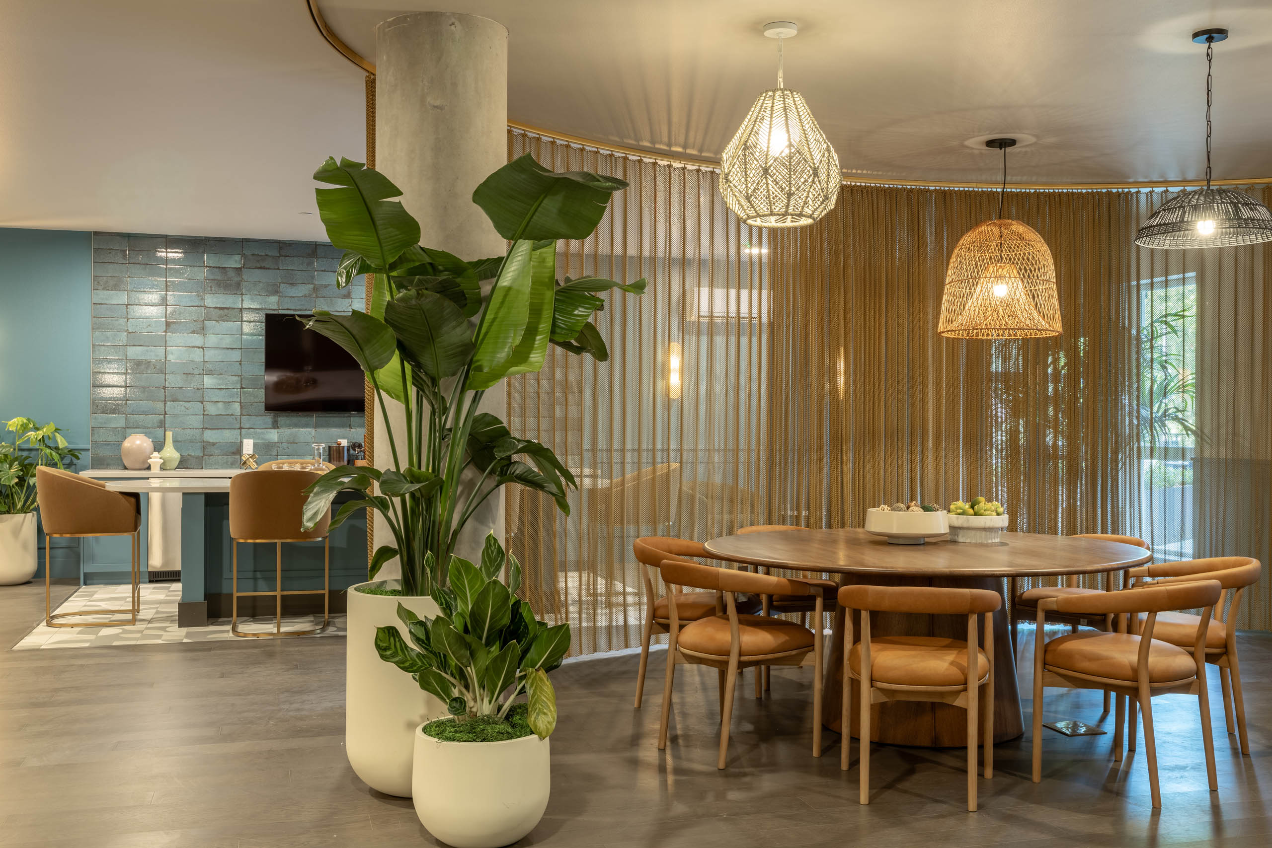 Havana Lounge with a round wood table, leather chairs, woven pendant lighting, tall potted plants, and bar seating area in the background.