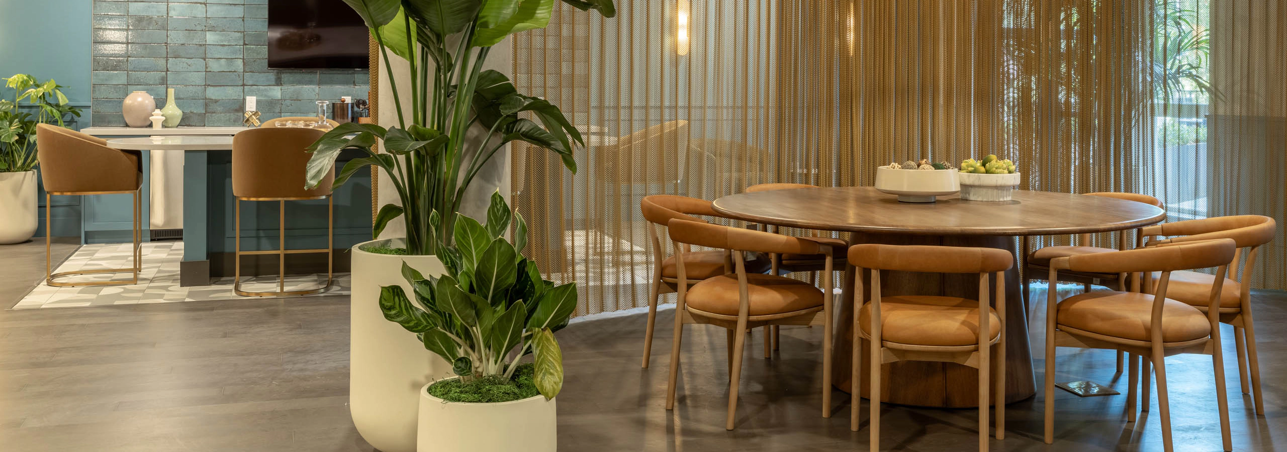 Havana Lounge with a round wood table, leather chairs, woven pendant lighting, tall potted plants, and bar seating area in the background.
