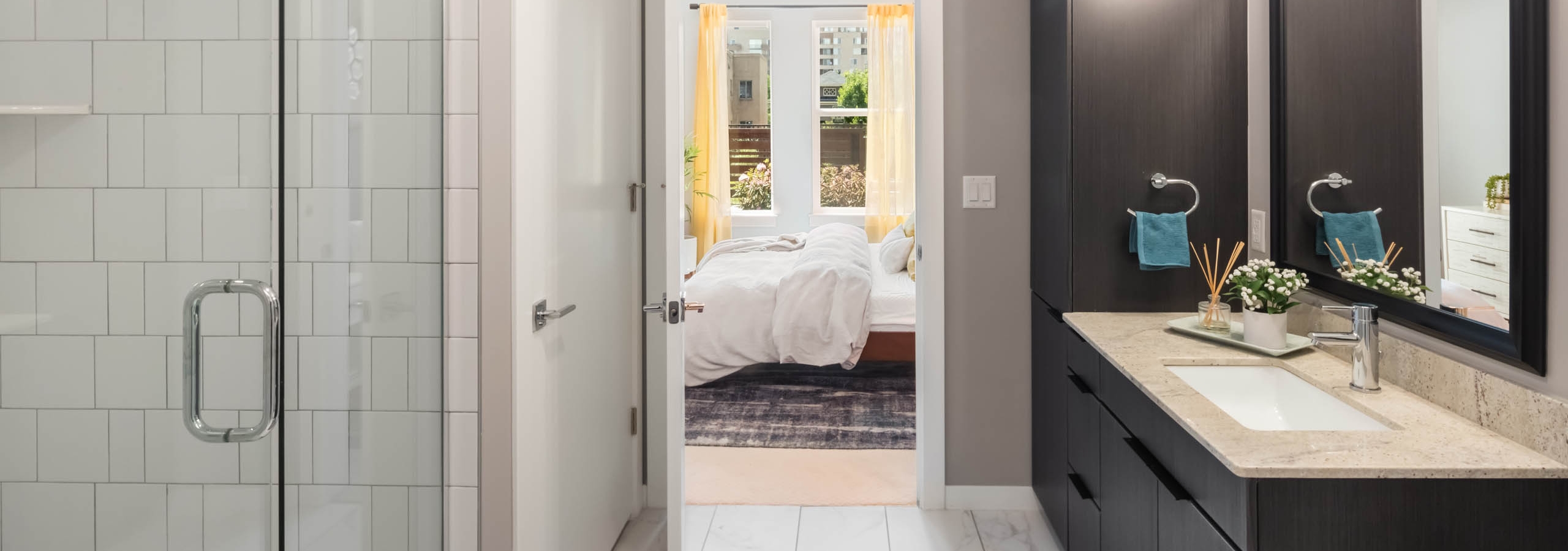 AMLI at Uptown spacious apartment bathroom with a subway tiled shower and marble tiled floors featuring dark wood cabinetry