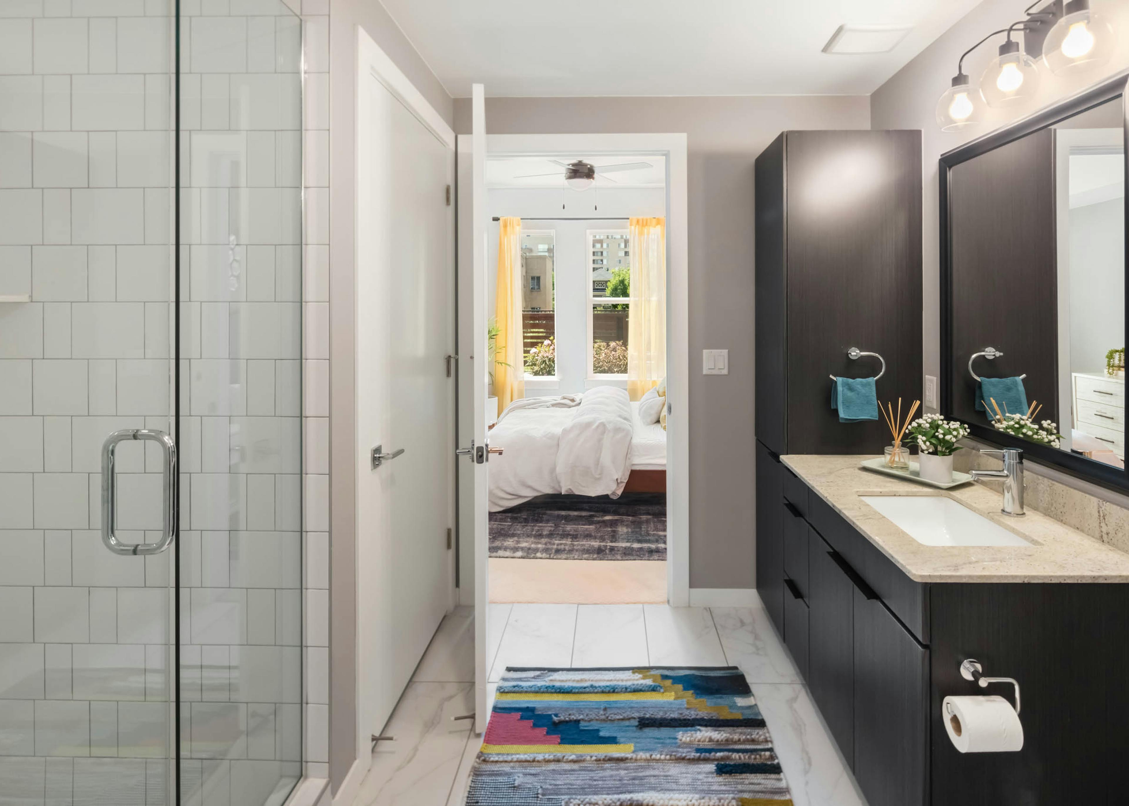 AMLI at Uptown spacious apartment bathroom with a subway tiled shower and marble tiled floors featuring dark wood cabinetry