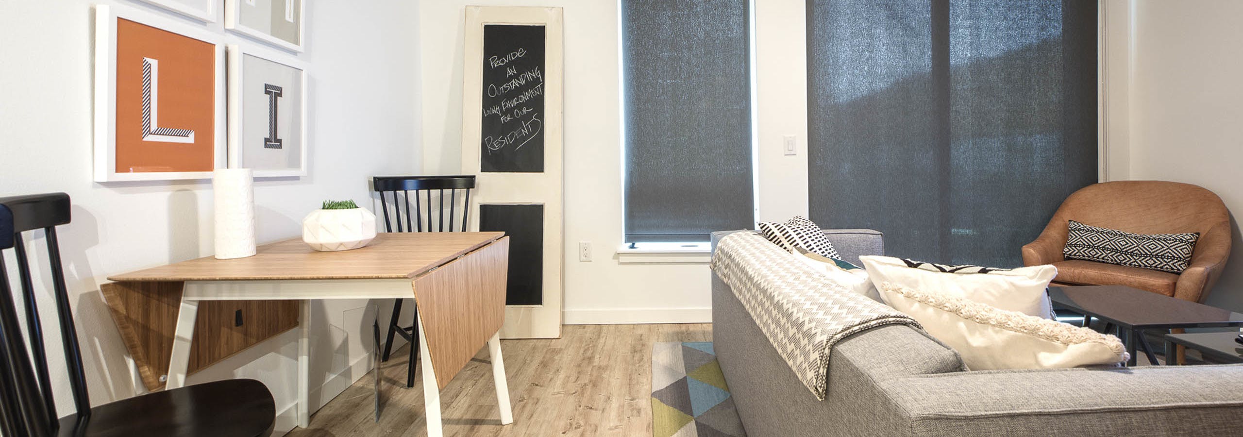 Interior AMLI Wallingford apartment living room with kitchen table and two chairs with a grey couch and solar shades