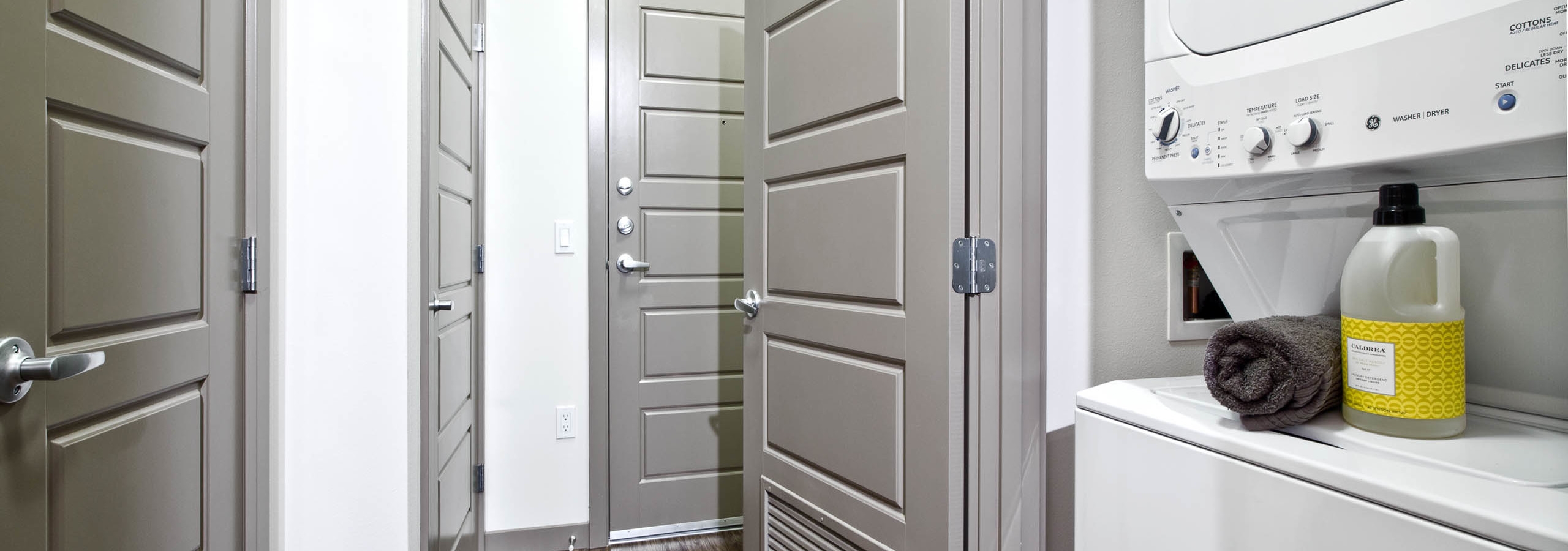 Interior view of stackable washer and dryer at AMLI Mark24 apartment with view of front entrance