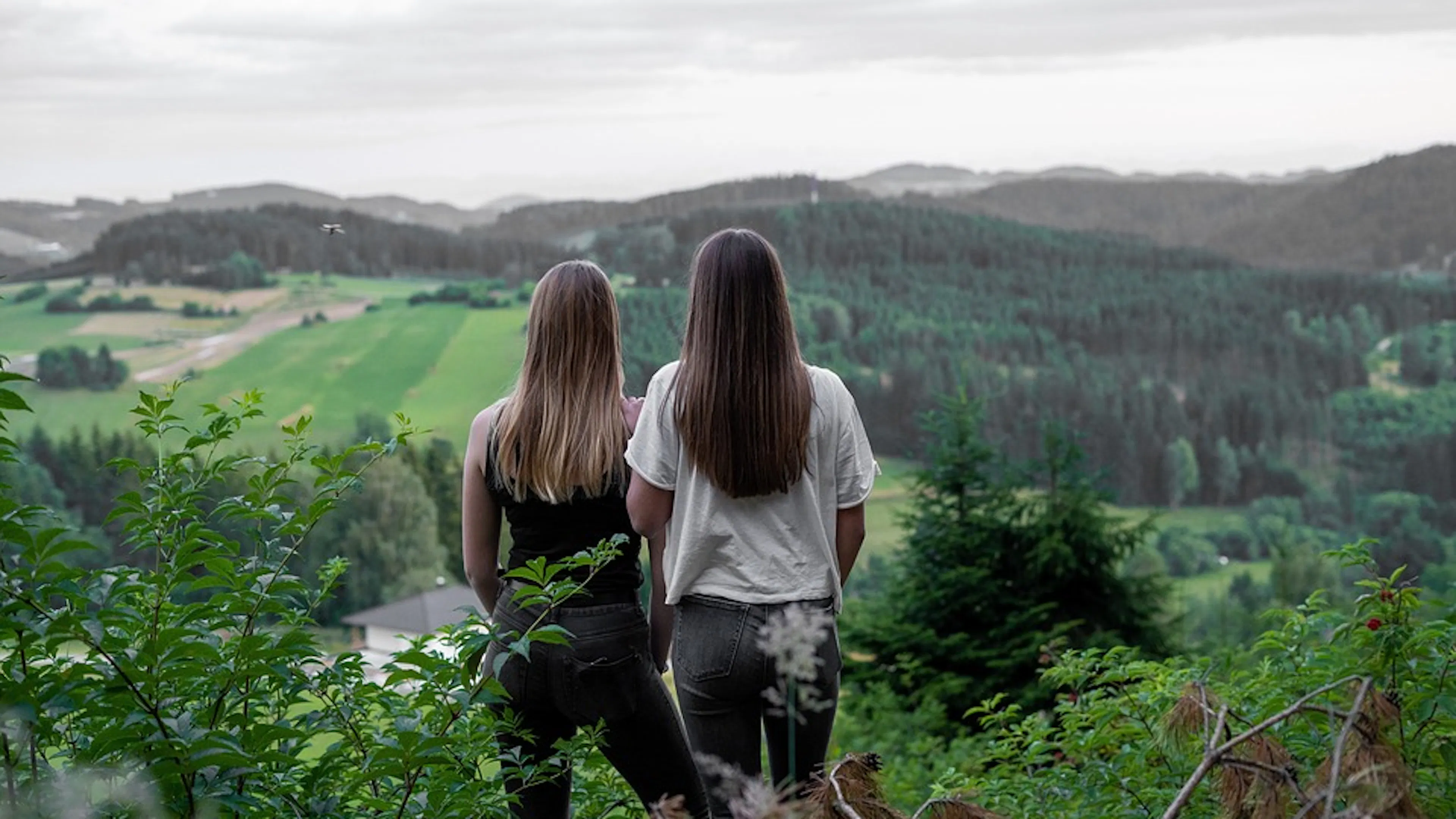 Two women facing away from the camera toward a valley and rolling green hills