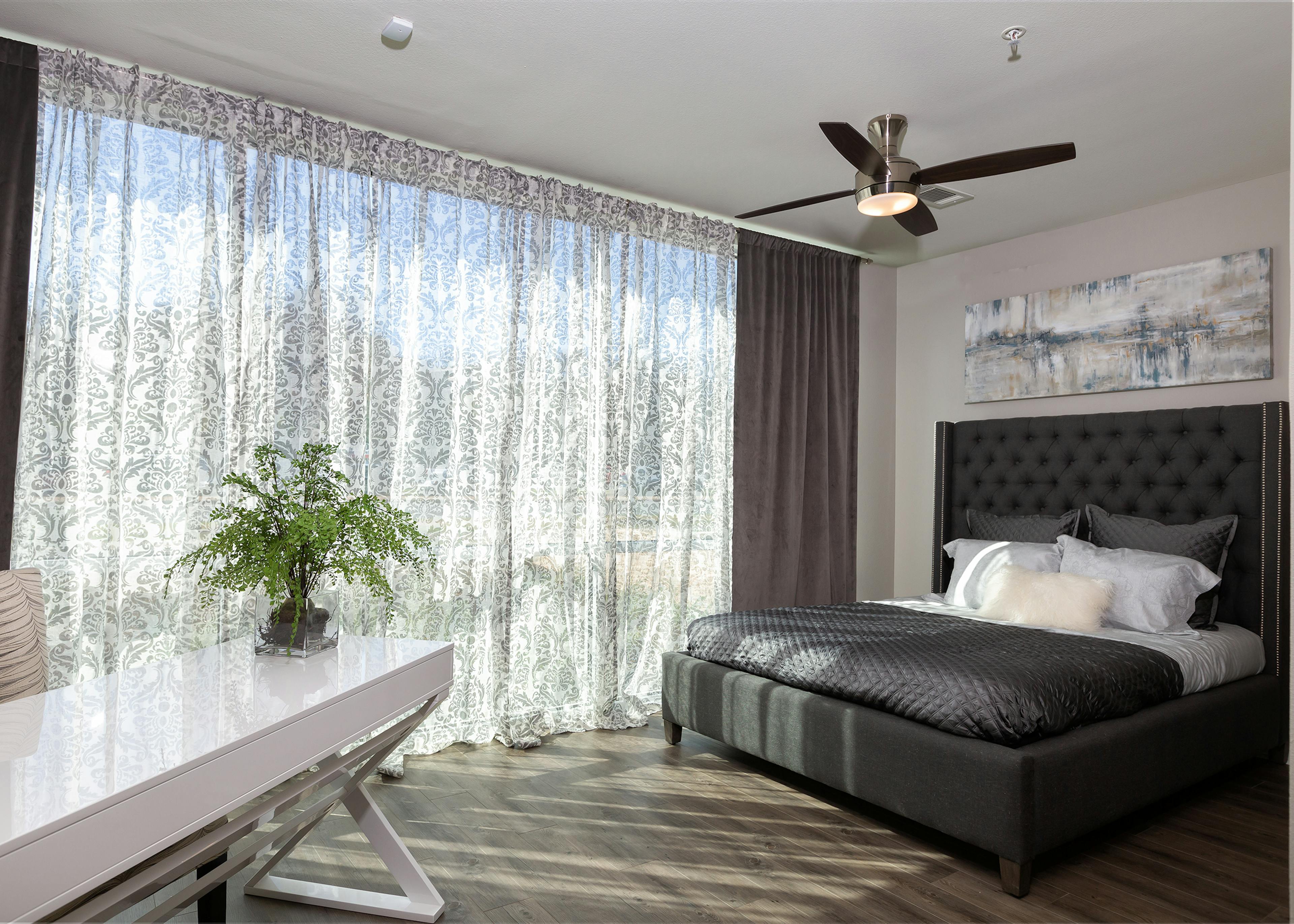 View of AMLI South Shore bedroom with grey headboard on bed showing dark floors and white desk with floor to ceiling windows