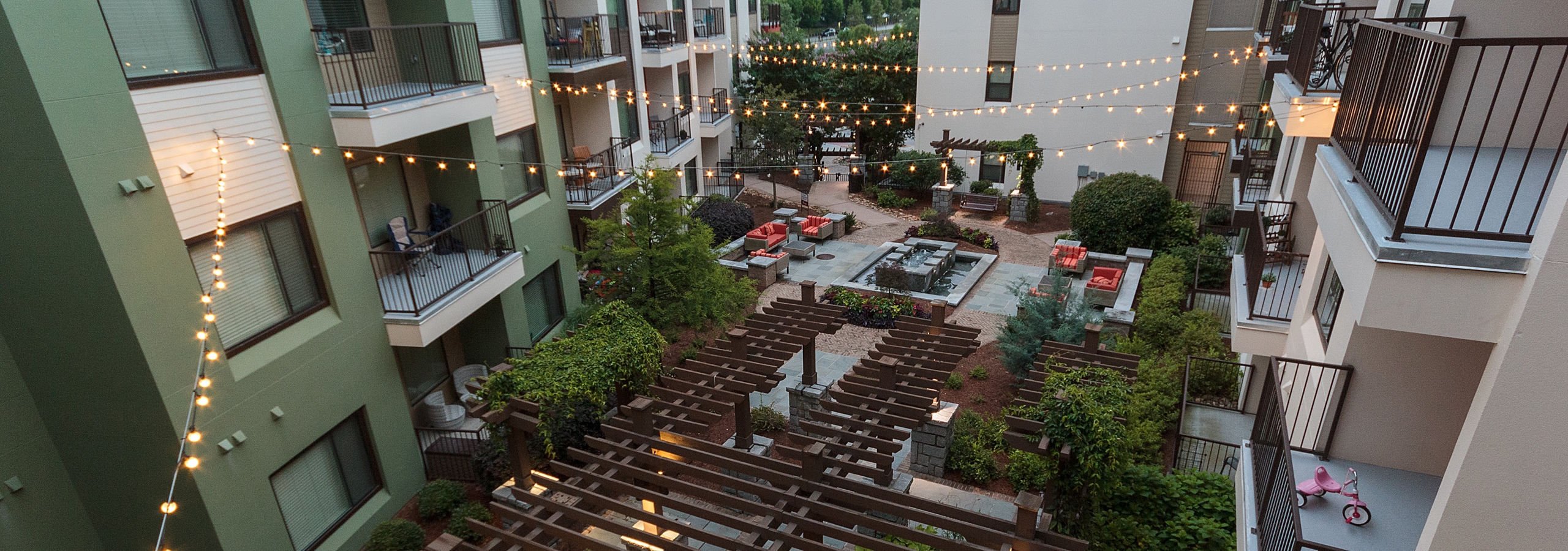 Overhead dusk view of AMLI Ponce Park courtyard  with sitting area and fountainand lit hanging lights