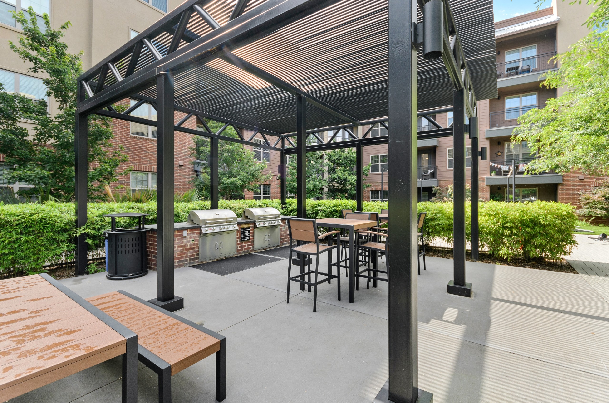 AMLI Grapevine apartments outdoor shaded grill station with two stainless grills and outdoor seating surrounded by shrubbery
