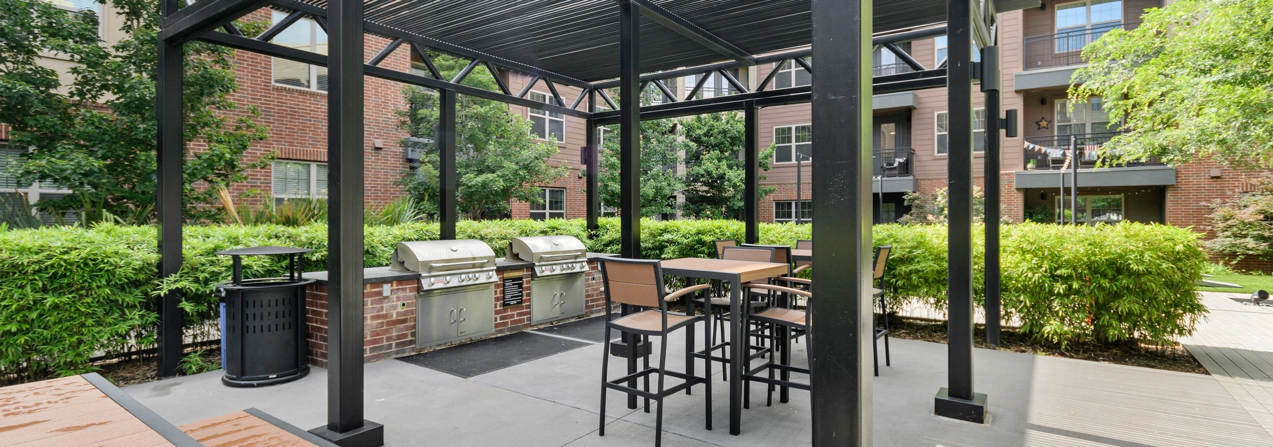 AMLI Grapevine apartments outdoor shaded grill station with two stainless grills and outdoor seating surrounded by shrubbery