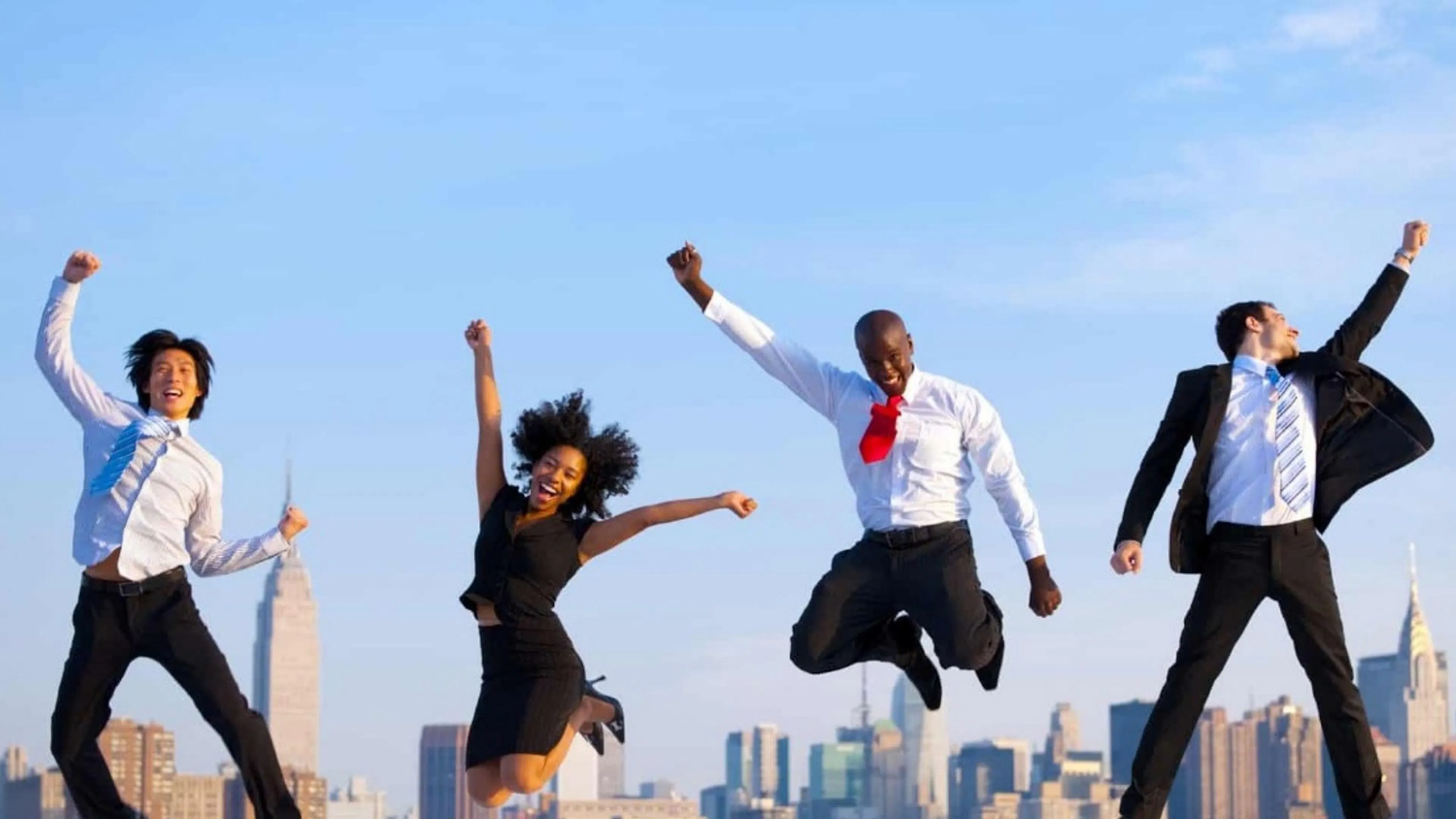 three men in suits and one woman in black dress jumping into the air