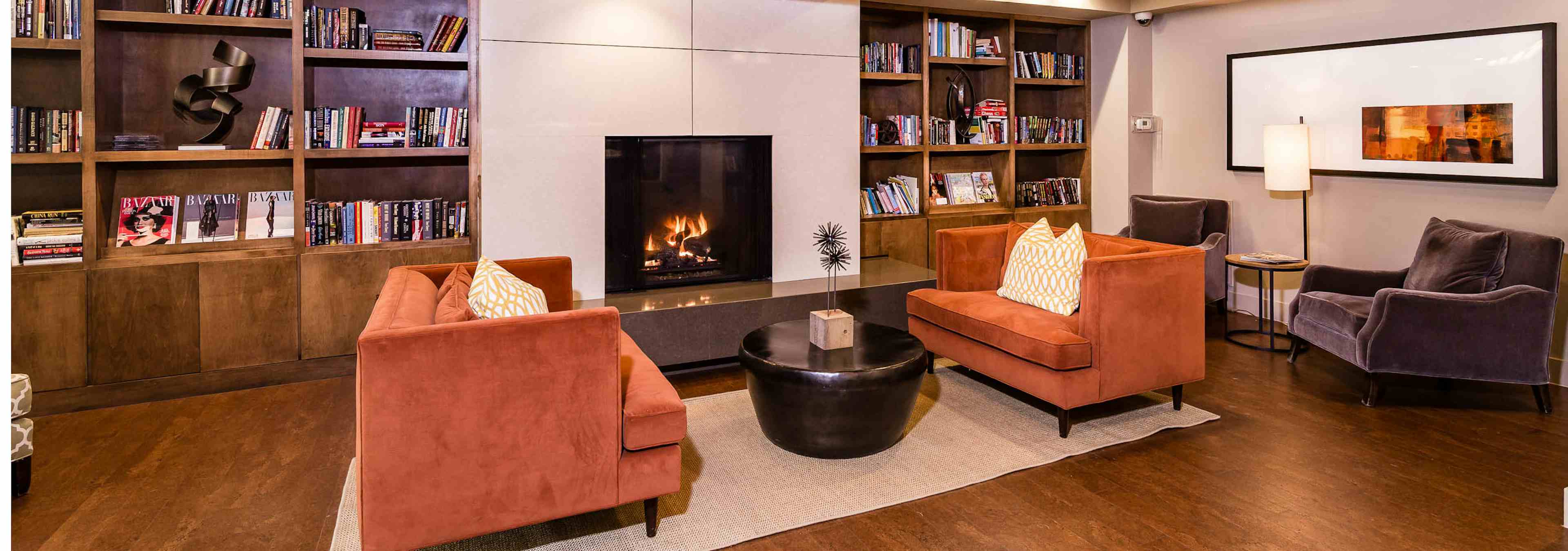 Interior view of library study lounge with two orange suede sofas, bookshelves and fireplace at AMLI RidgeGate apartments