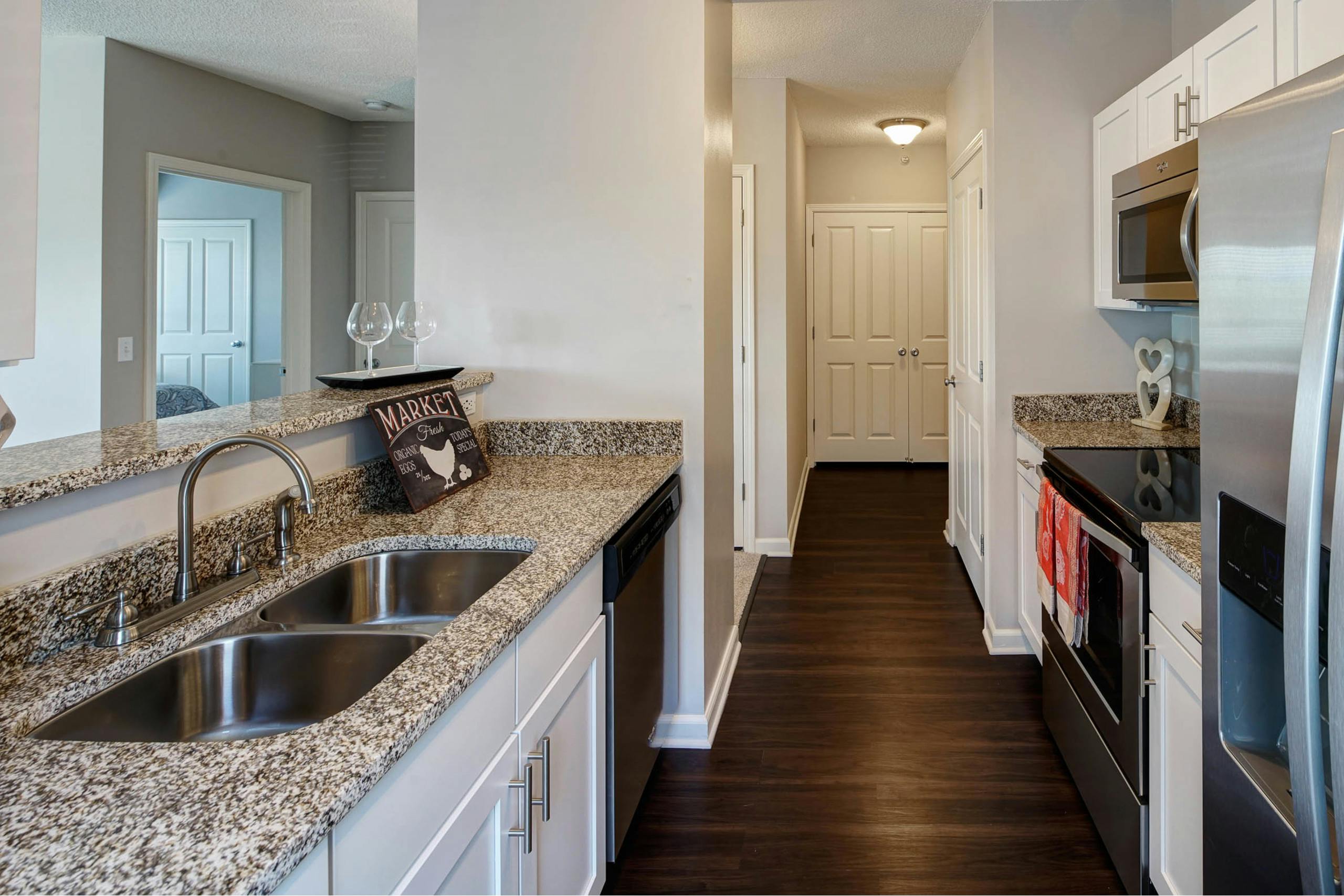 AMLI at Seven Bridges kitchen with white cabinets and granite countertops with dark wood floors leading to a hallway