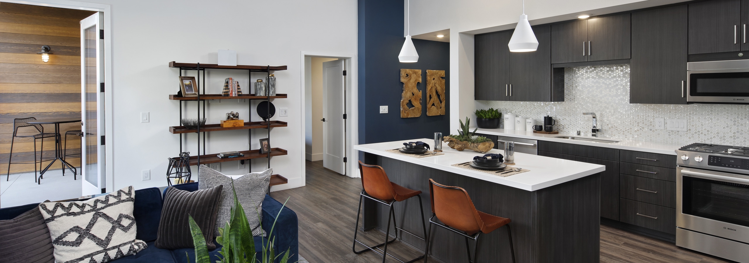 AMLI Marina Del Rey kitchen with dark cabinetry, quartz countertop and pendant lighting and peek into living room and patio