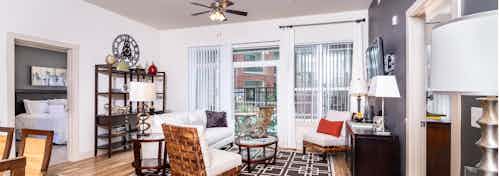 A living room at AMLI Park Avenue apartments with a white couch and a shelves and lamps and a television and a balcony door