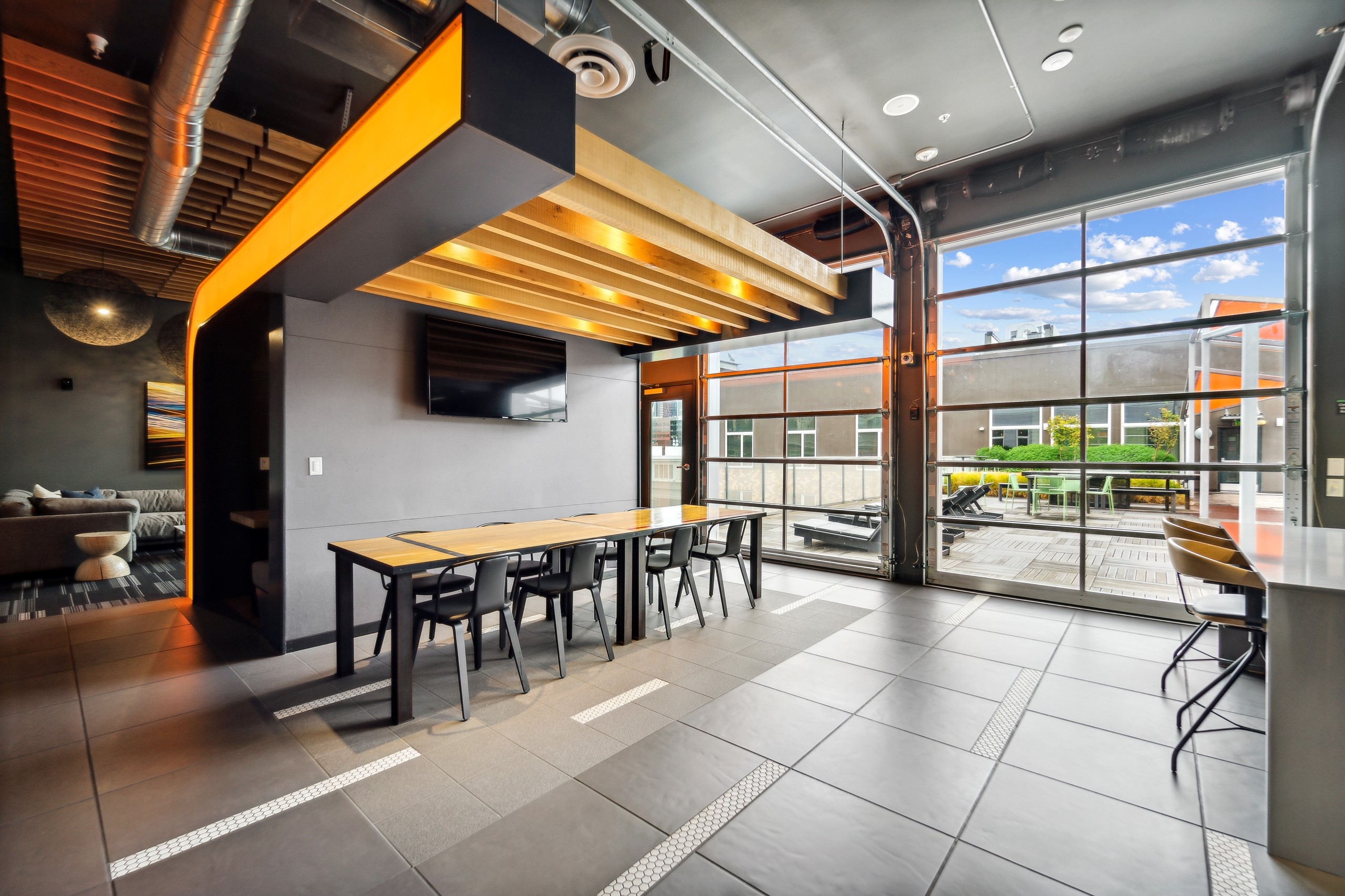 Rooftop lounge at AMLI South Lake Union with a long table with 8 chairs as well as two glass garage doors with outdoor view