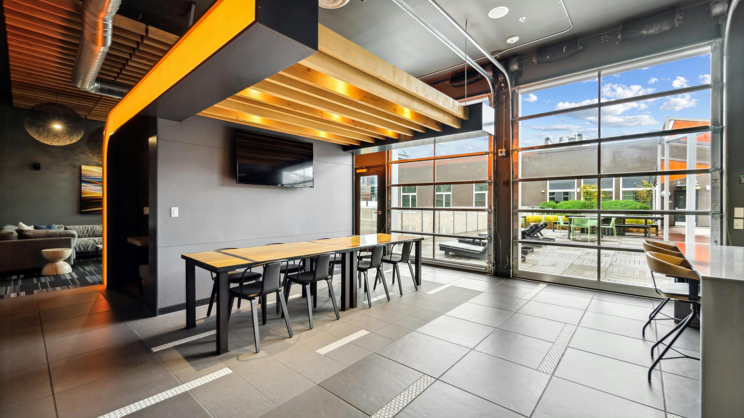 Rooftop lounge at AMLI South Lake Union with a long table with 8 chairs as well as two glass garage doors with outdoor view