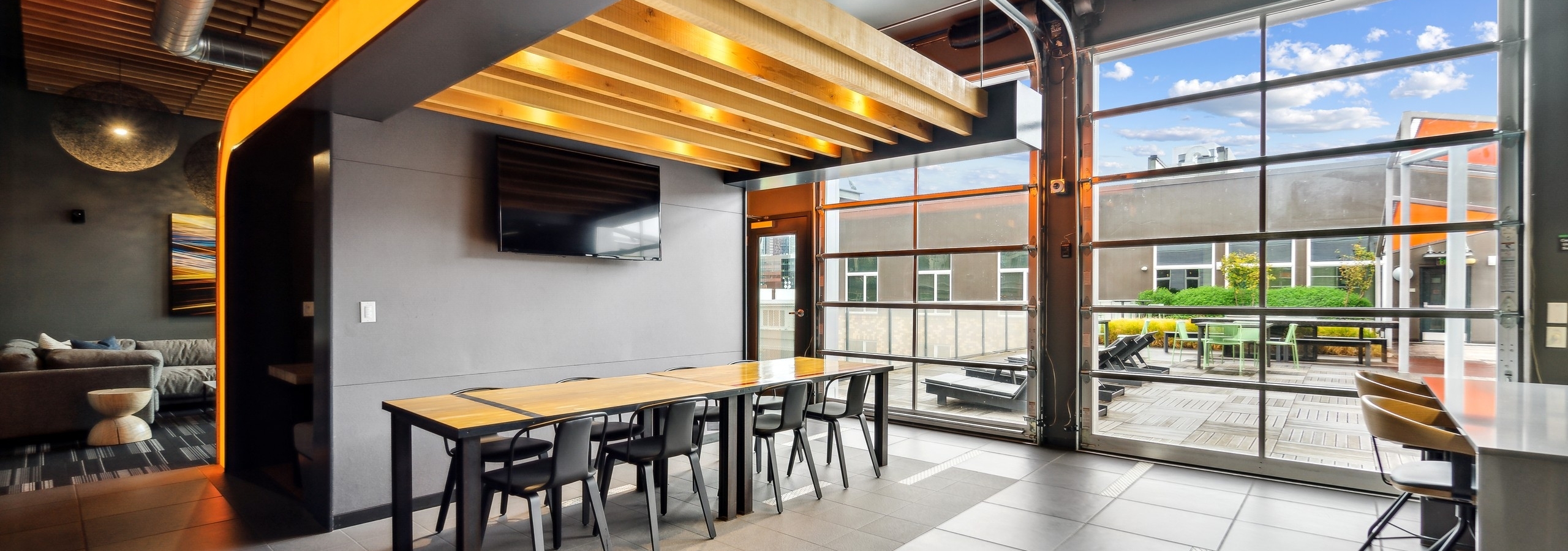 Rooftop lounge at AMLI South Lake Union with a long table with 8 chairs as well as two glass garage doors with outdoor view