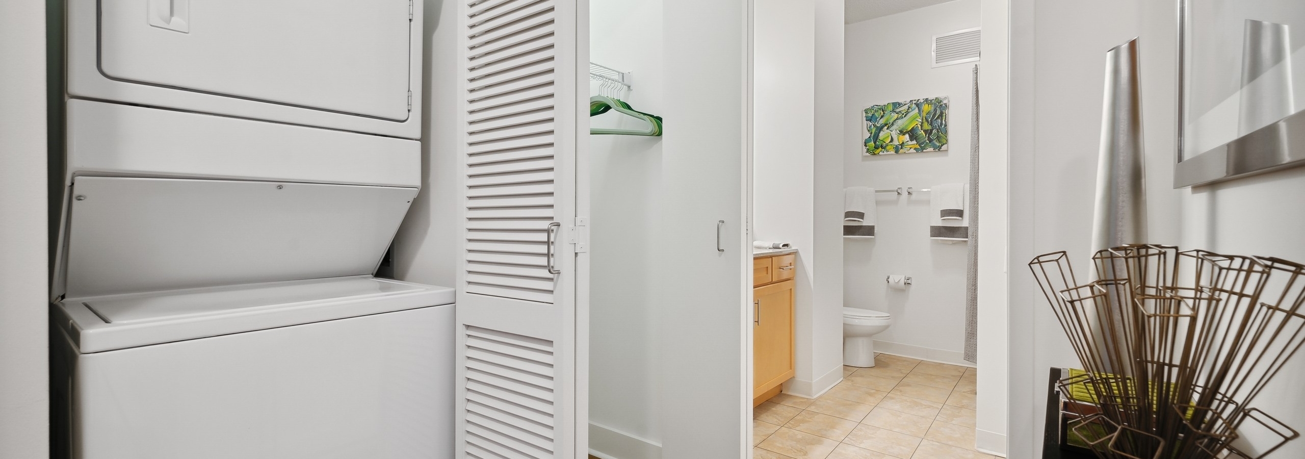 White stackable washer and dryer with closet door open and view of closet and bathroom with tile floor at AMLI 900 apartments