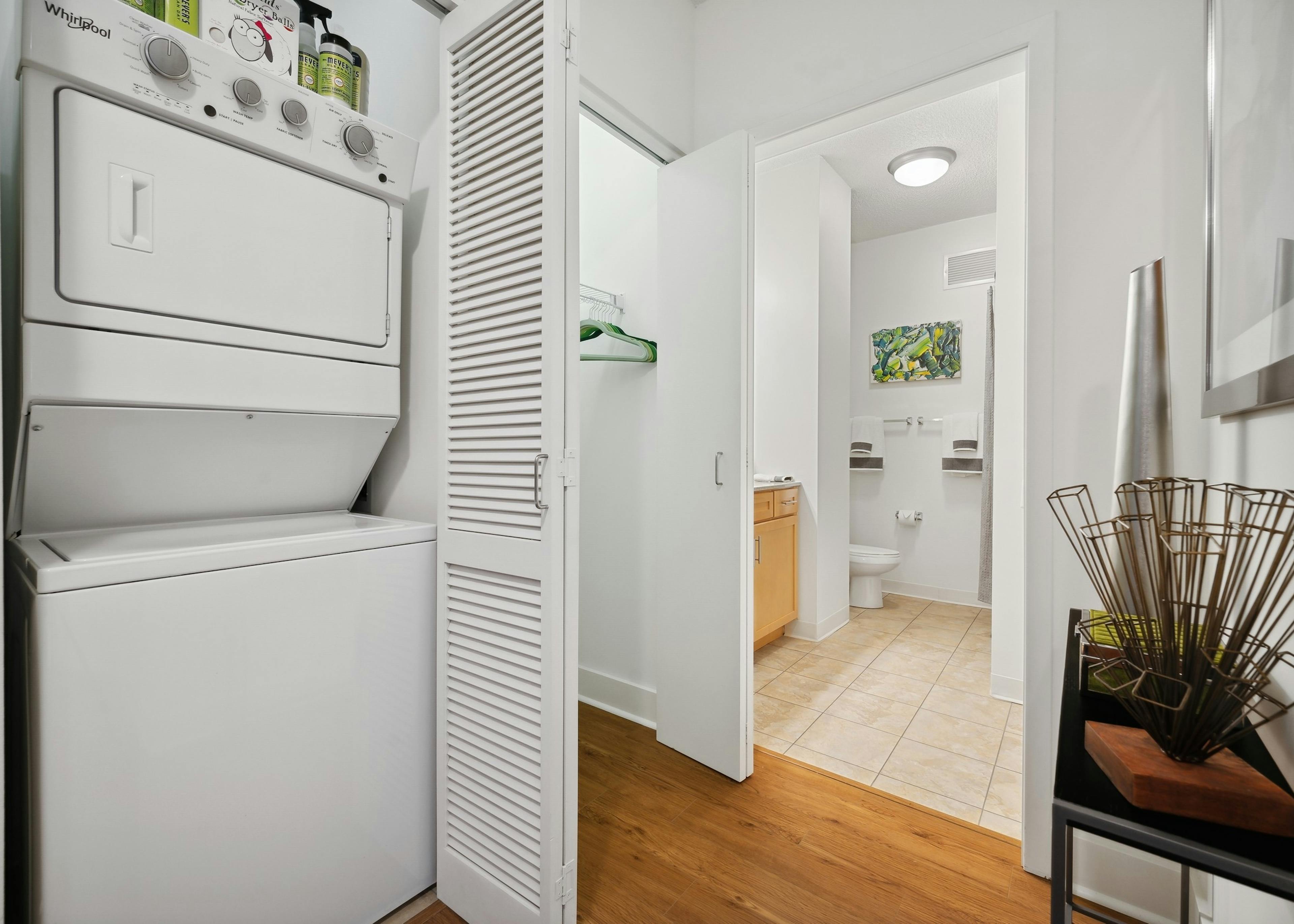 White stackable washer and dryer with closet door open and view of closet and bathroom with tile floor at AMLI 900 apartments