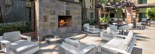 Large outdoor fireplace with cushioned lounge seating by outdoor grilling area at AMLI Warner Center apartments