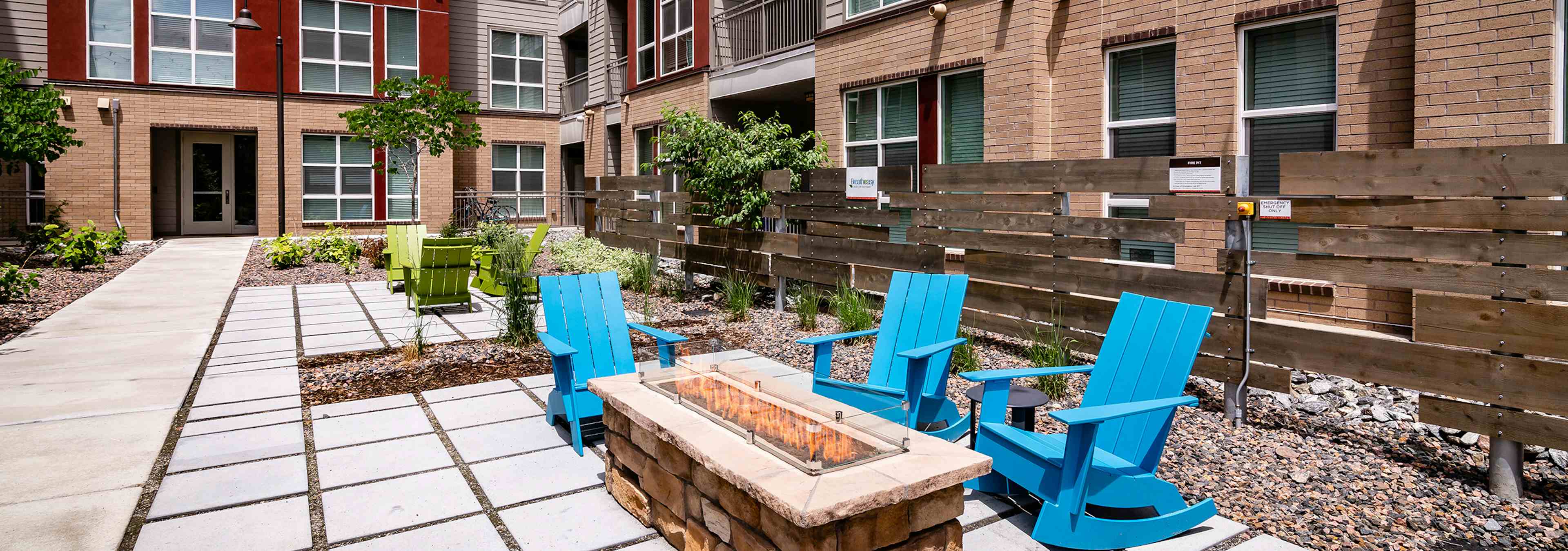 Courtyard fire pit area at AMLI Dry Creek apartments with wooden rocking chairs and a fence and surrounding scrubs and trees