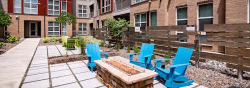 Courtyard fire pit area at AMLI Dry Creek apartments with wooden rocking chairs and a fence and surrounding scrubs and trees