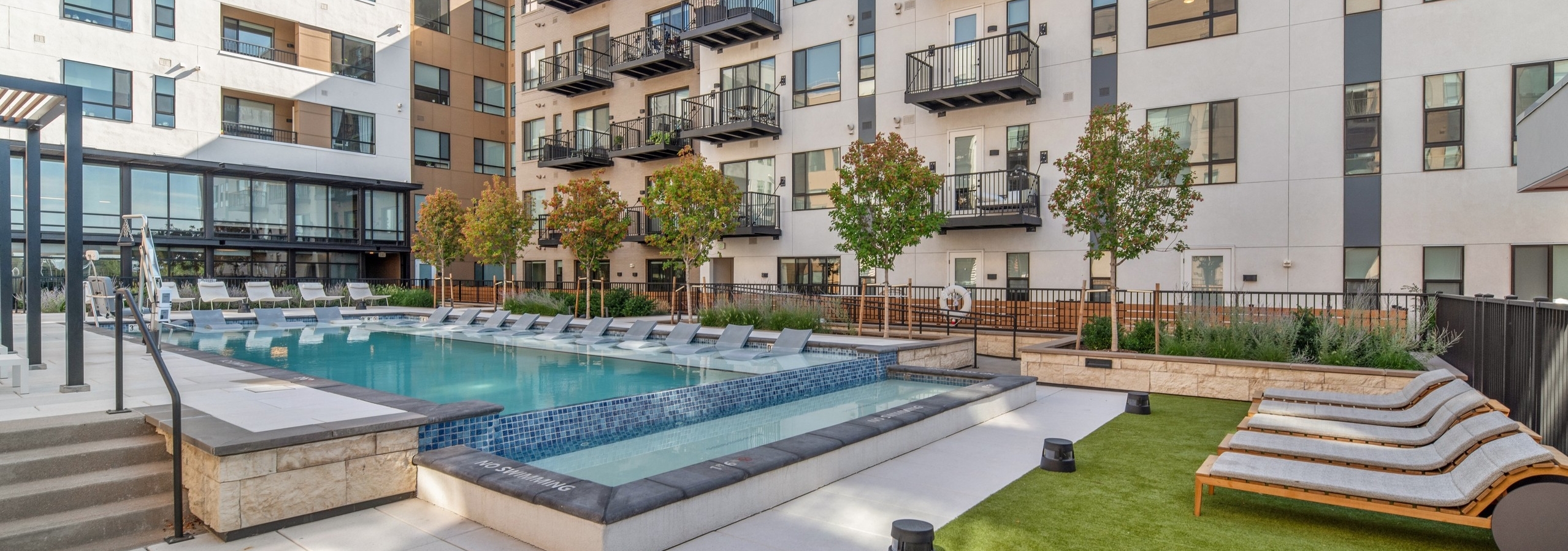Courtyard pool at AMLI Broadway Park with lounge chairs and green grass with black metal rail fence surrounded by building
