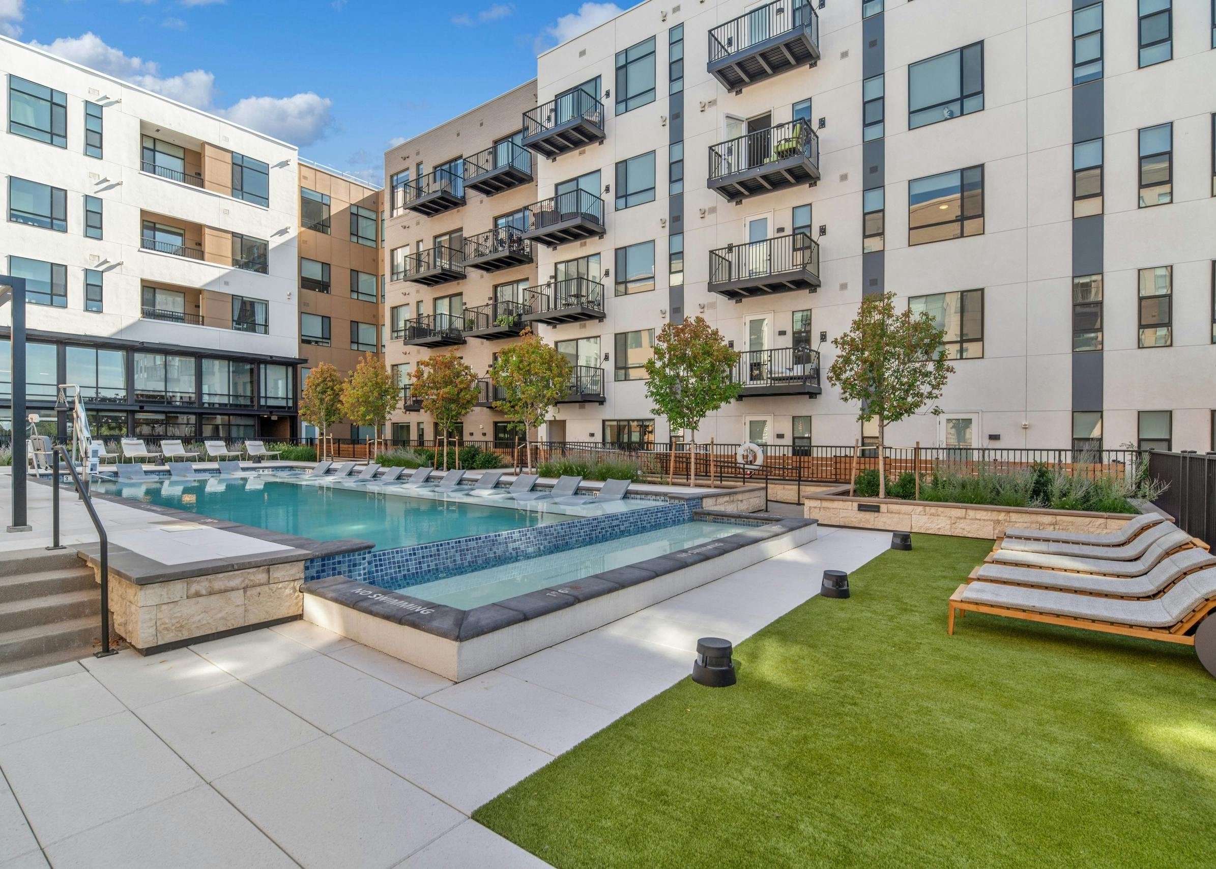 Courtyard pool at AMLI Broadway Park with lounge chairs and green grass with black metal rail fence surrounded by building