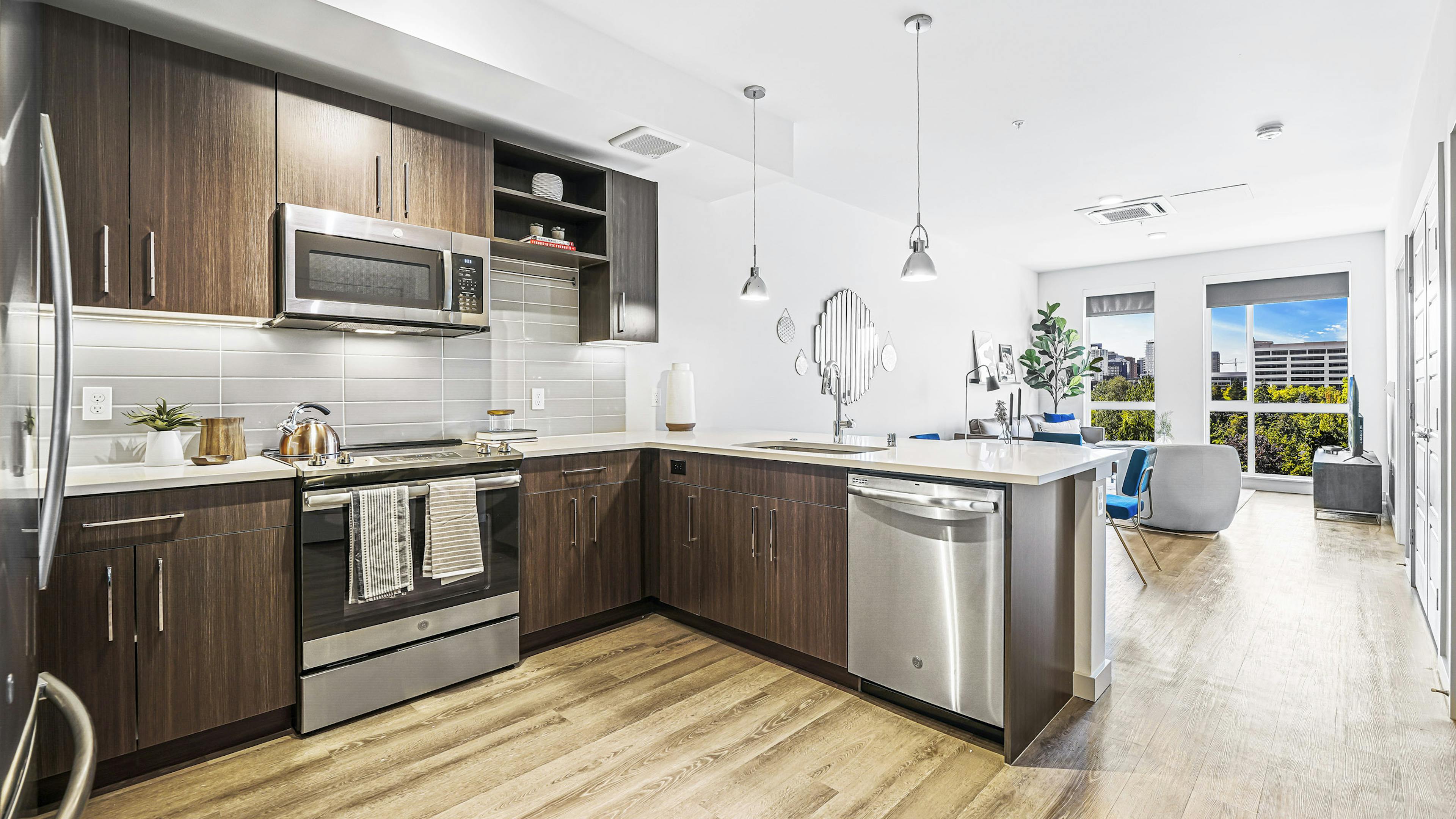 AMLI Spring District apartment kitchen with dark brown cabinets and light gray tile backsplash and view of living room