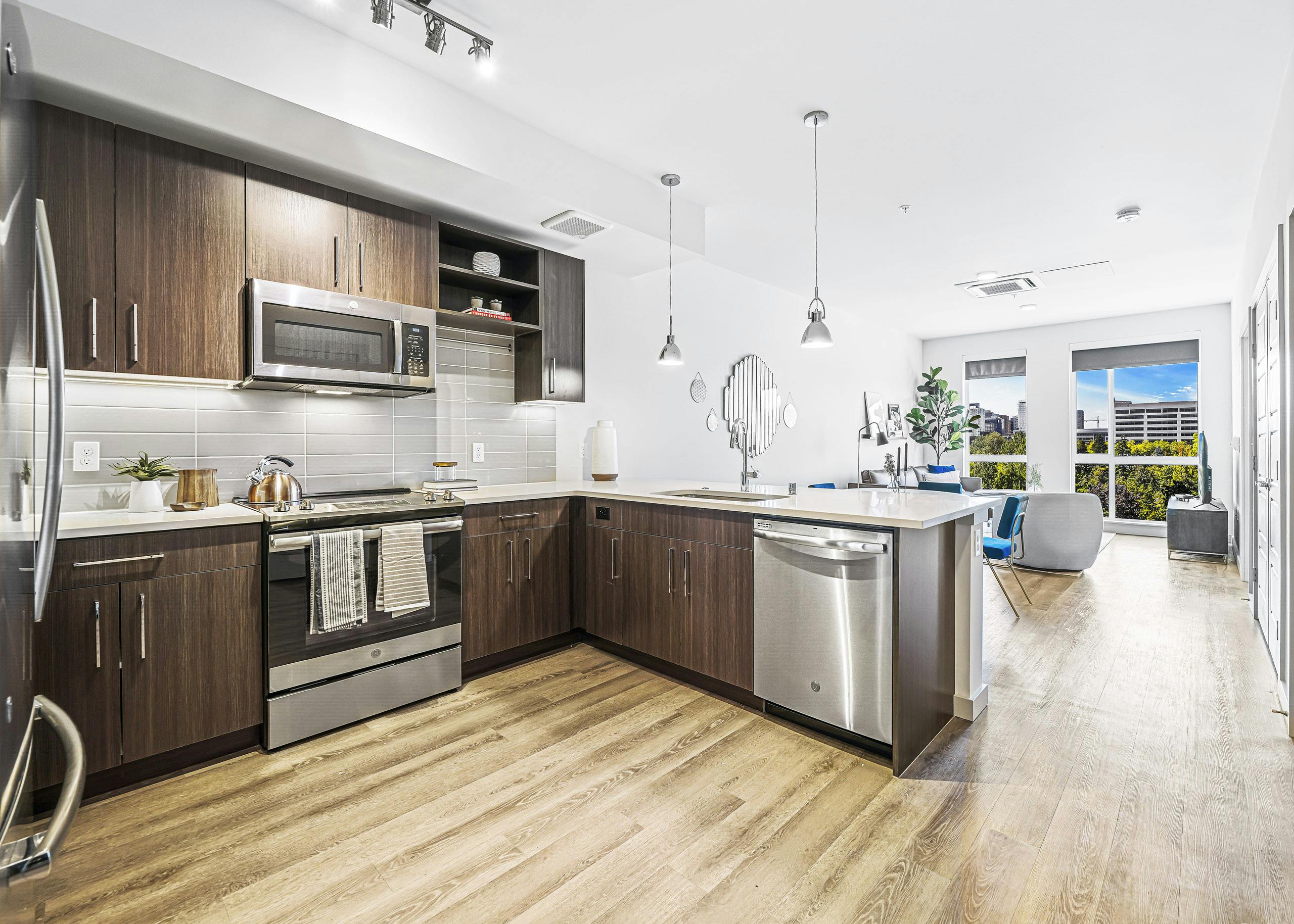 AMLI Spring District apartment kitchen with dark brown cabinets and light gray tile backsplash and view of living room