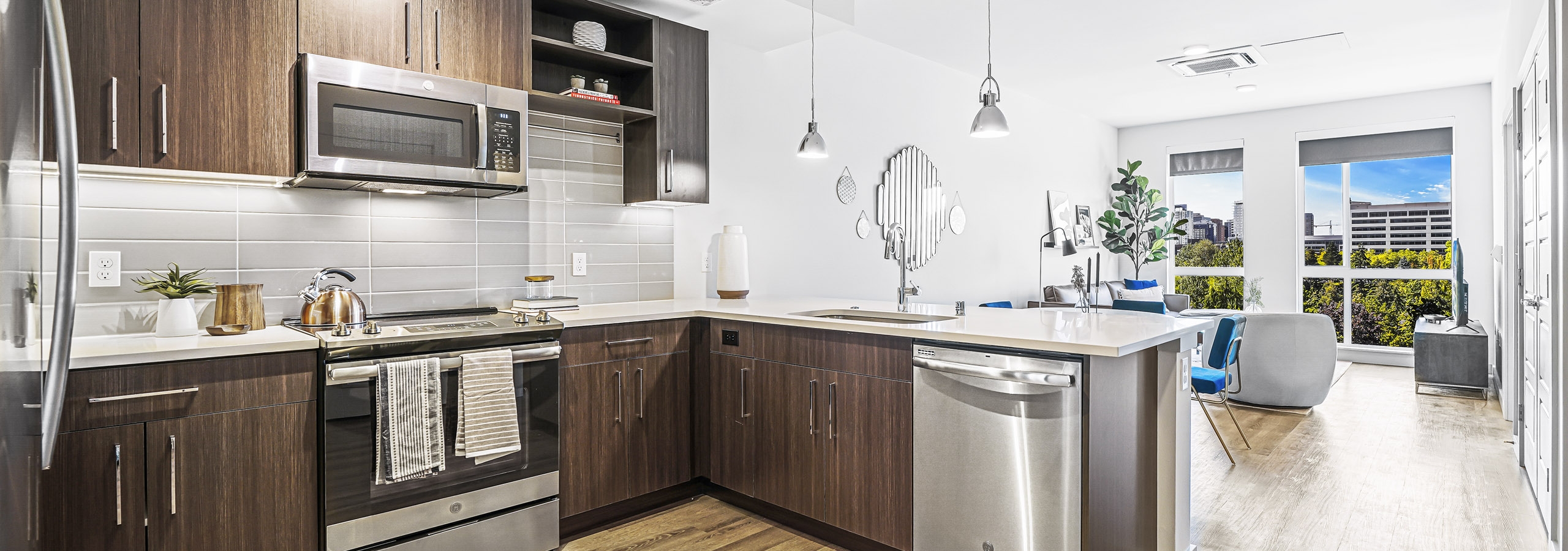 AMLI Spring District apartment kitchen with dark brown cabinets and light gray tile backsplash and view of living room