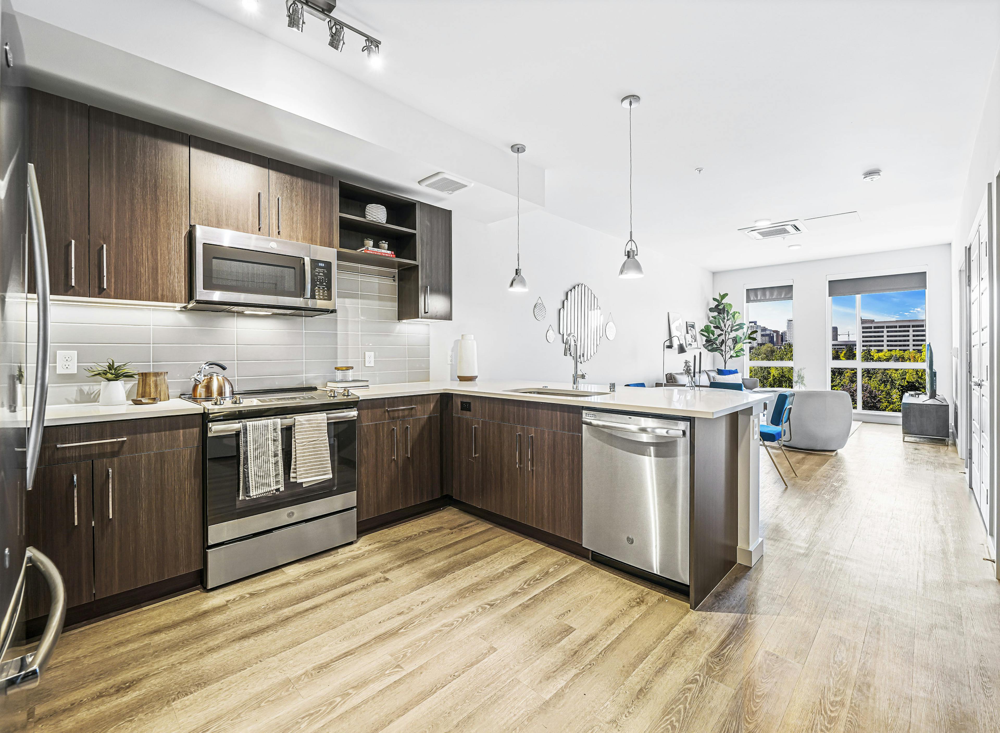 AMLI Spring District apartment kitchen with dark brown cabinets and light gray tile backsplash and view of living room