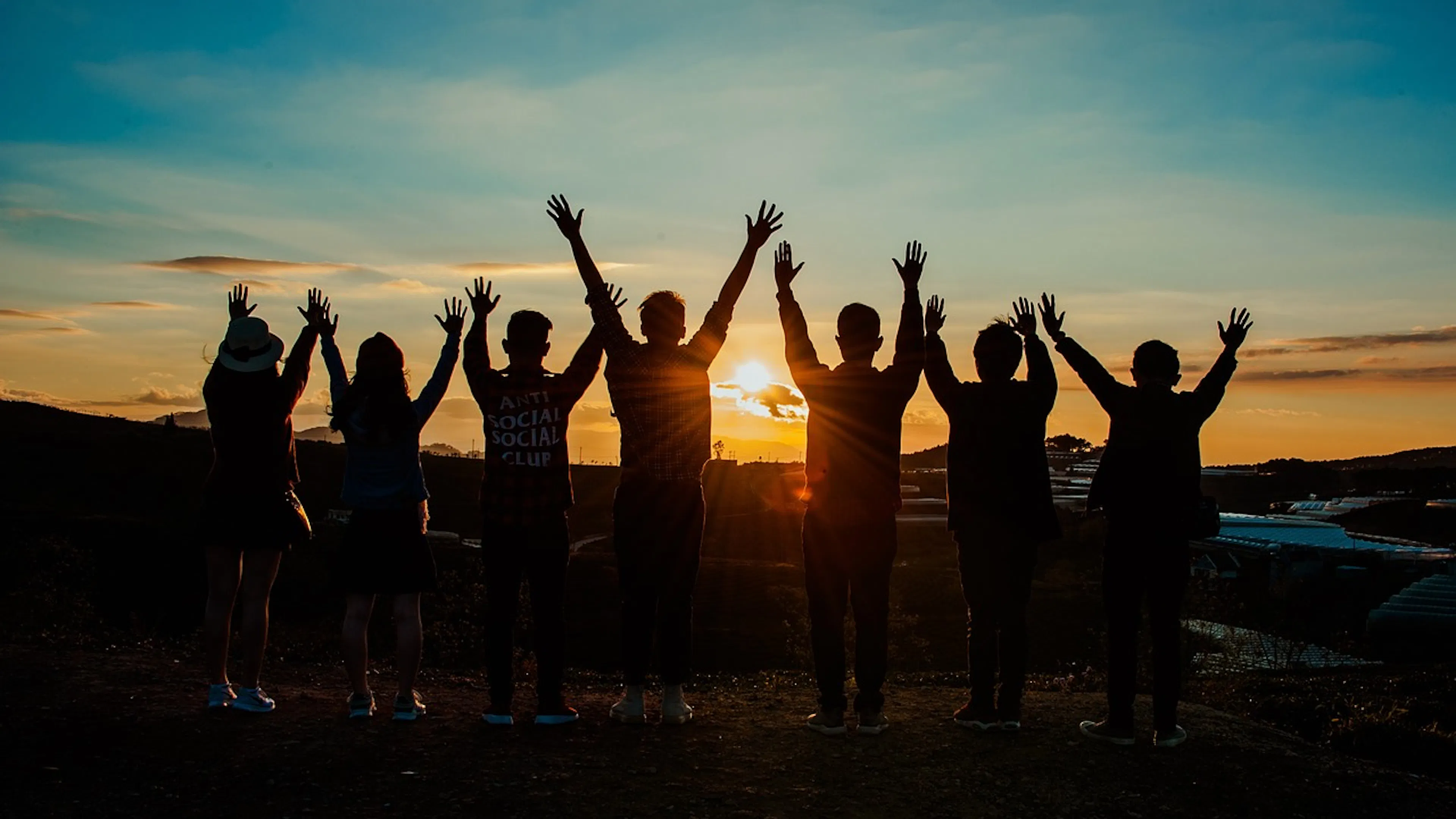 sunset with people standing in a line with hands raised