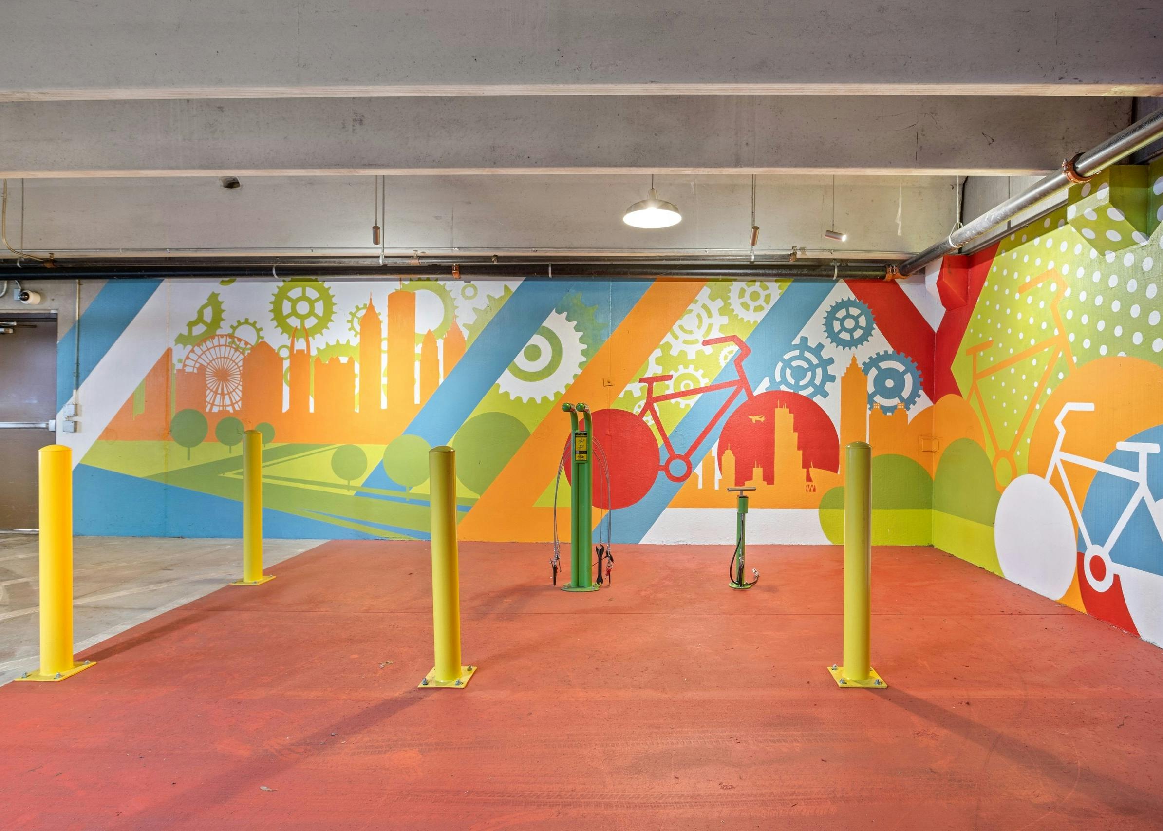 AMLI Ponce Park bike repair area with orange floor and colorful bike mural with green repair station and 4 yellow poles