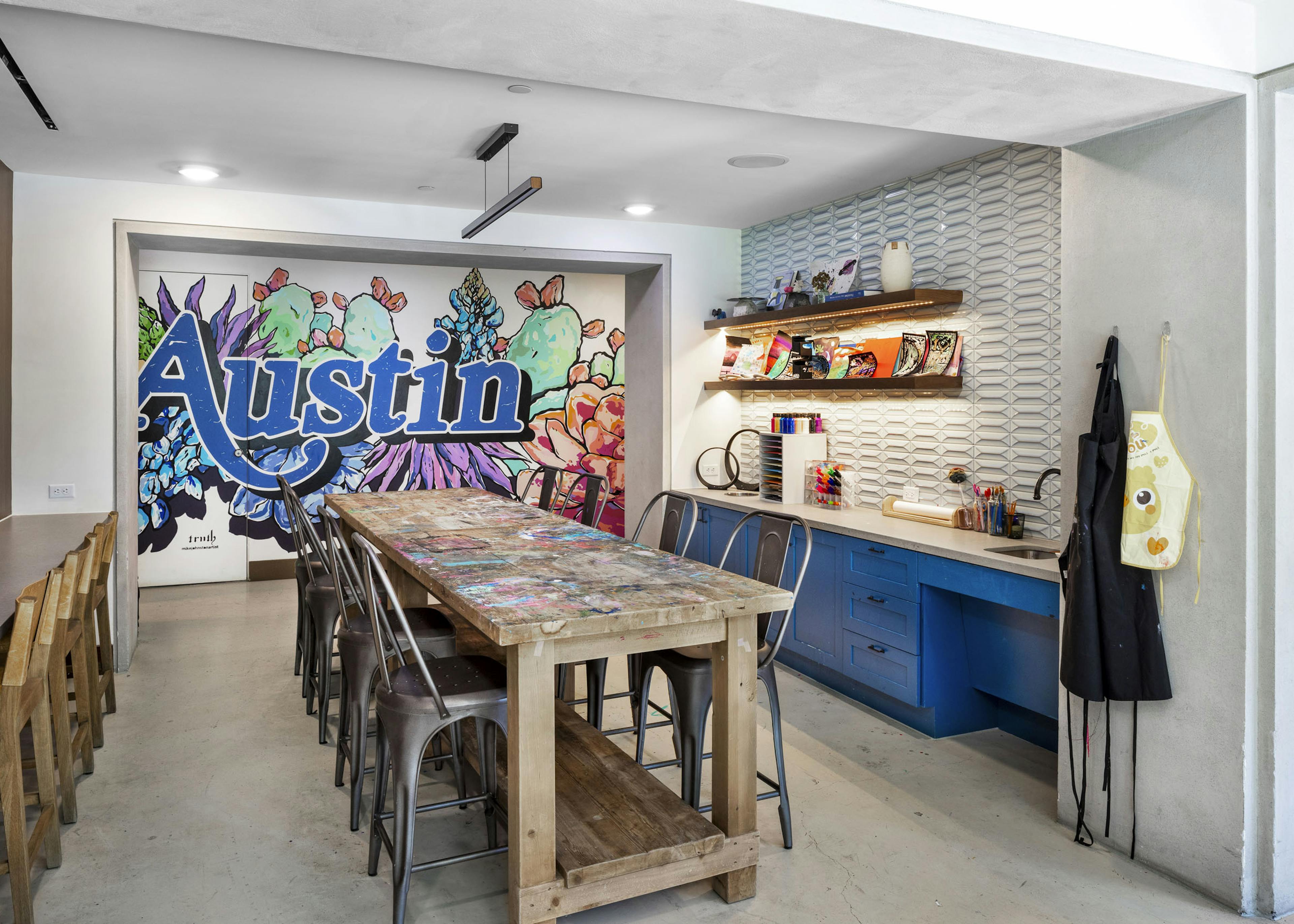 AMLI Lakeline maker space with a colorful Austin mural and a long wooden table flanked by metal chairs and blue cabinetry