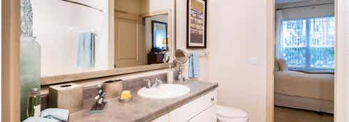 A bathroom at AMLI Park Avenue apartments with a large mirror and a granite counter top with sink and peek into the bedroom