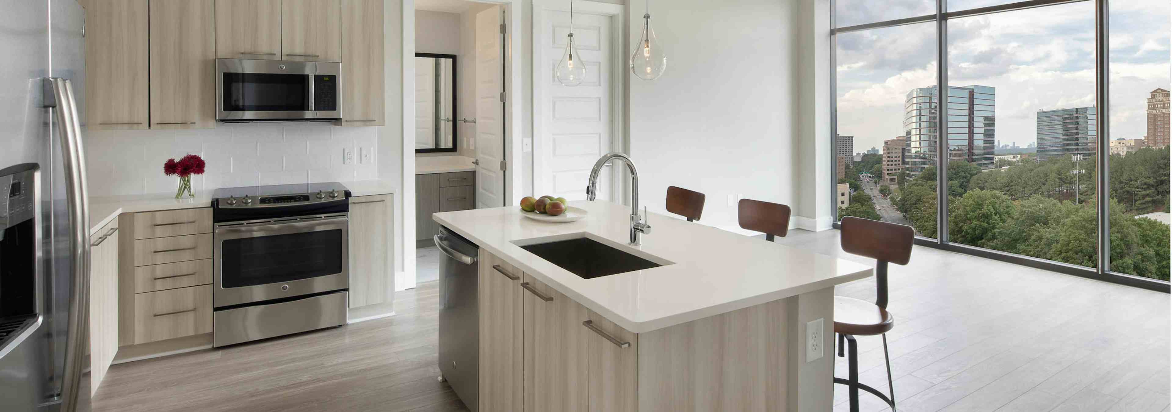 AMLI Arts Center kitchen with light wood cabinets and sleek white countertops connecting to living area with large windows