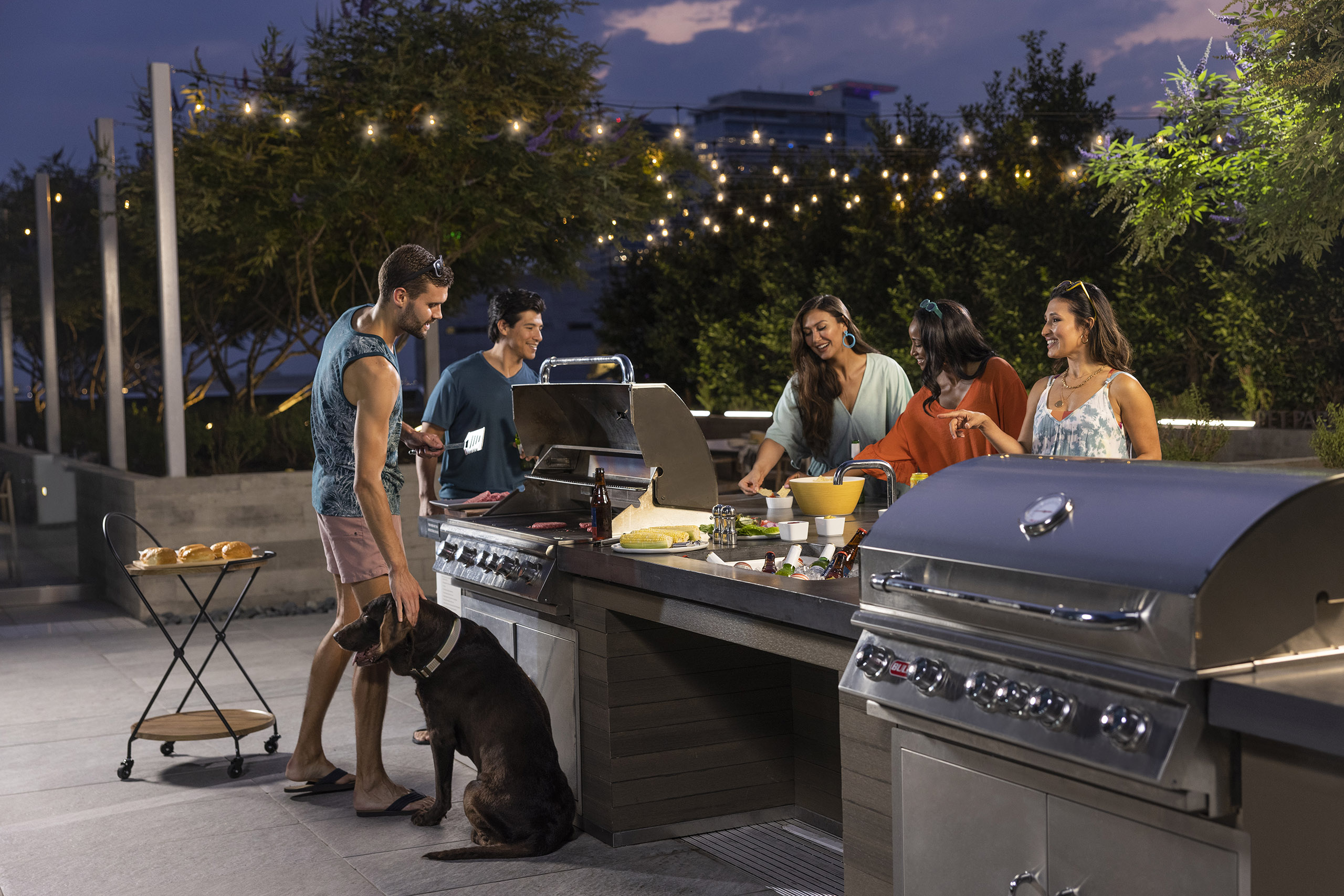 A group of friends cooking at AMLI Fountain Place outdoor grill area surrounded by greenery and under hanging lights